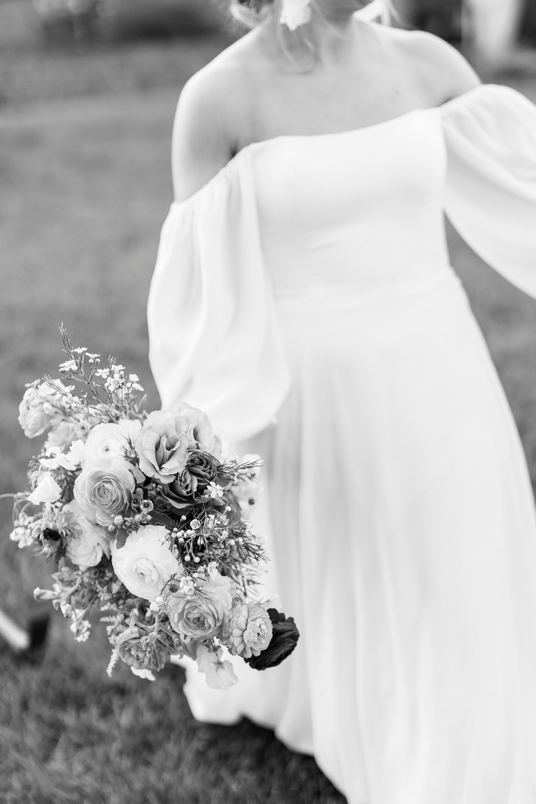 bride holds bouquet to side in off-the-shoulder wedding gown