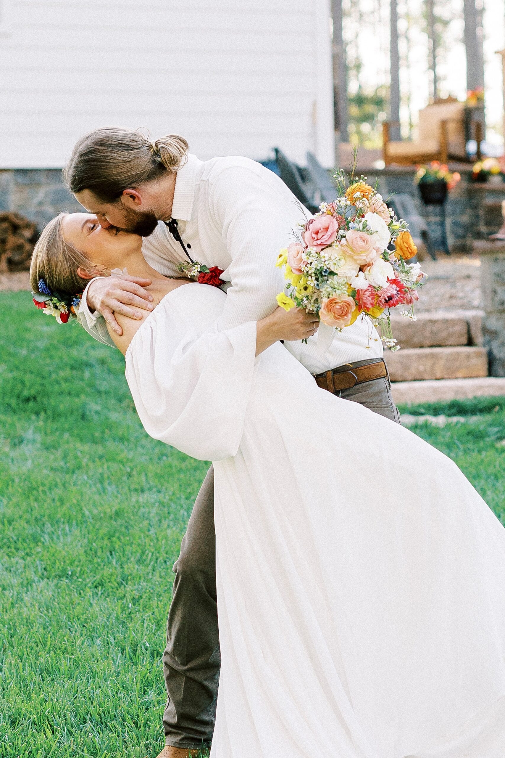 groom dips bride kissing her during wedding portraits on front lawn