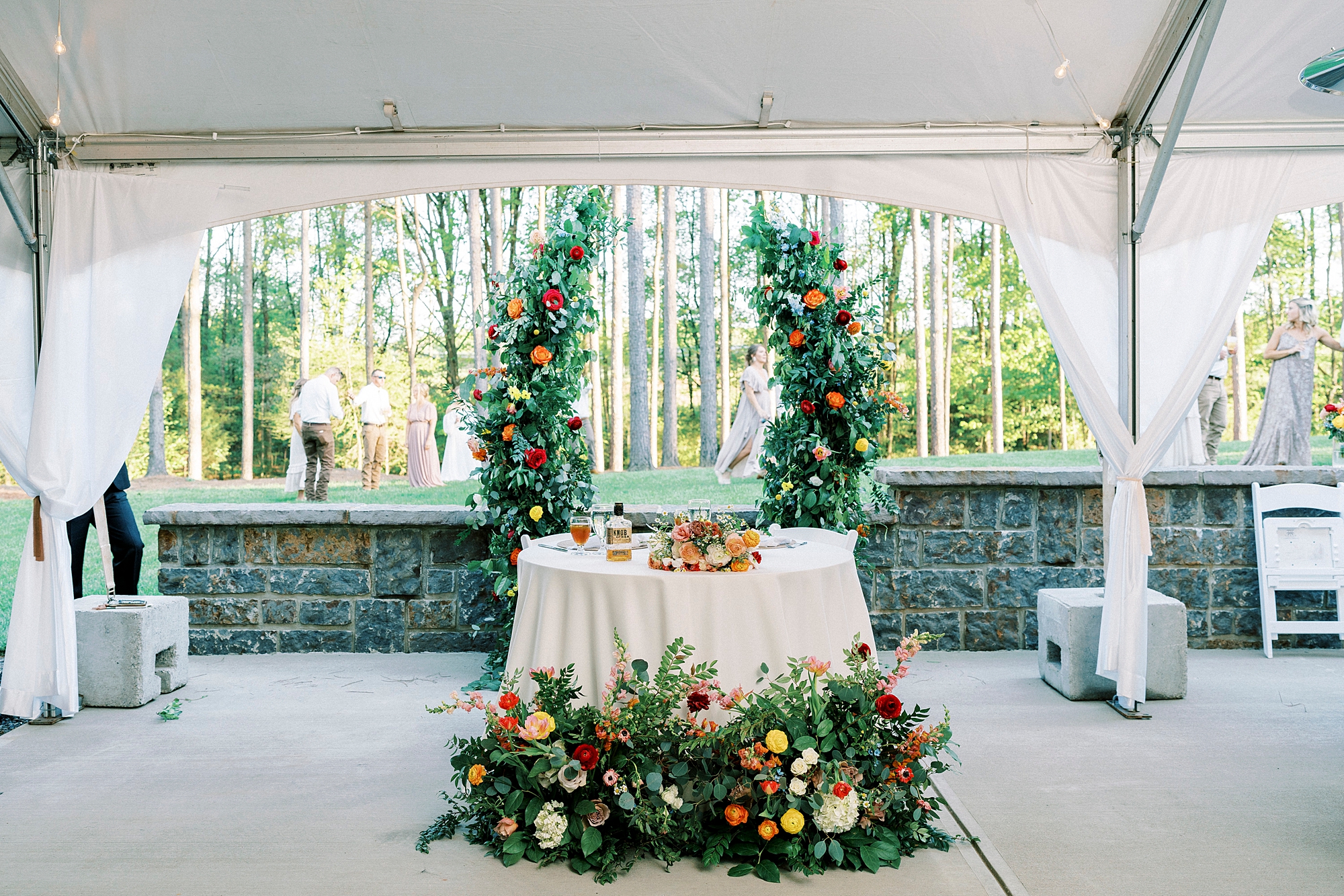 sweetheart table between two tall floral installations with greenery, yellow and pink flowers