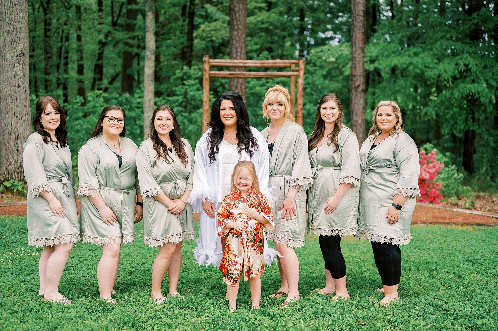 bride poses with bridesmaids in light green robes outside Danner Farms
