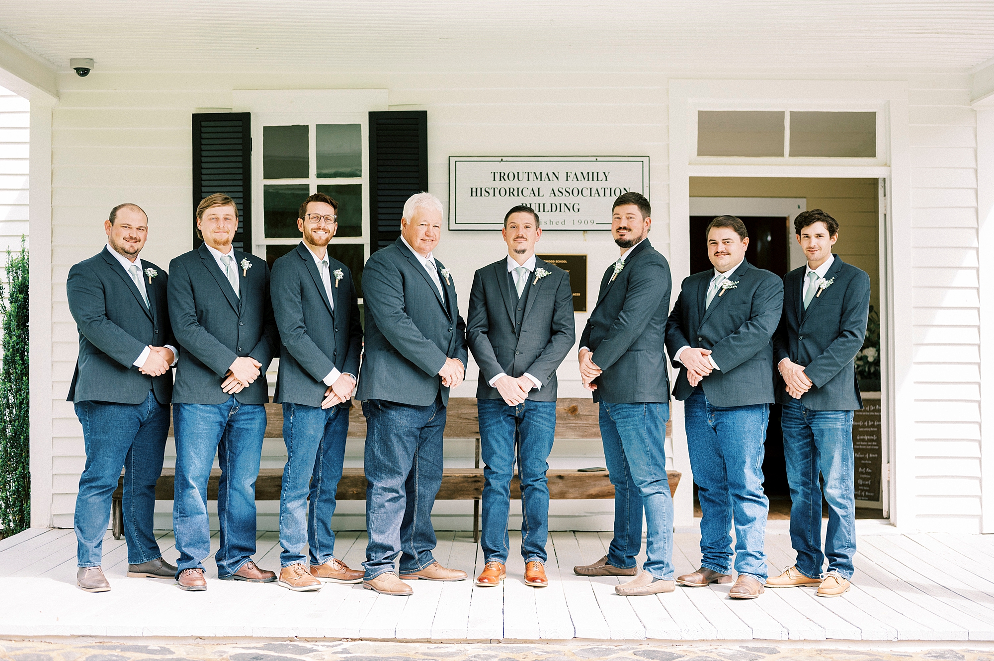 groom stands with groomsmen in navy suits outside white chapel at Danner Farms