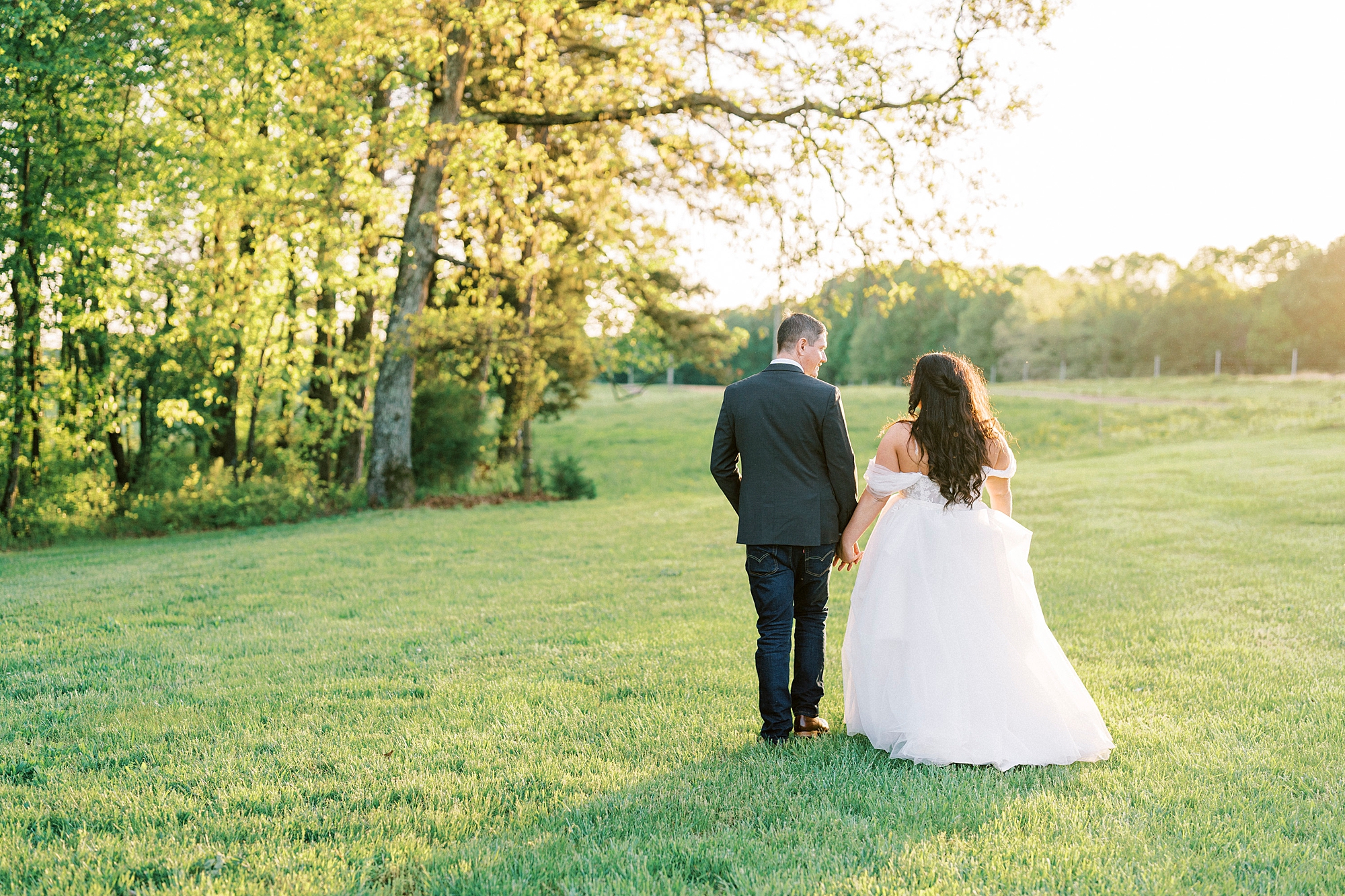 newlyweds walk away from photographer at sunset on lawn