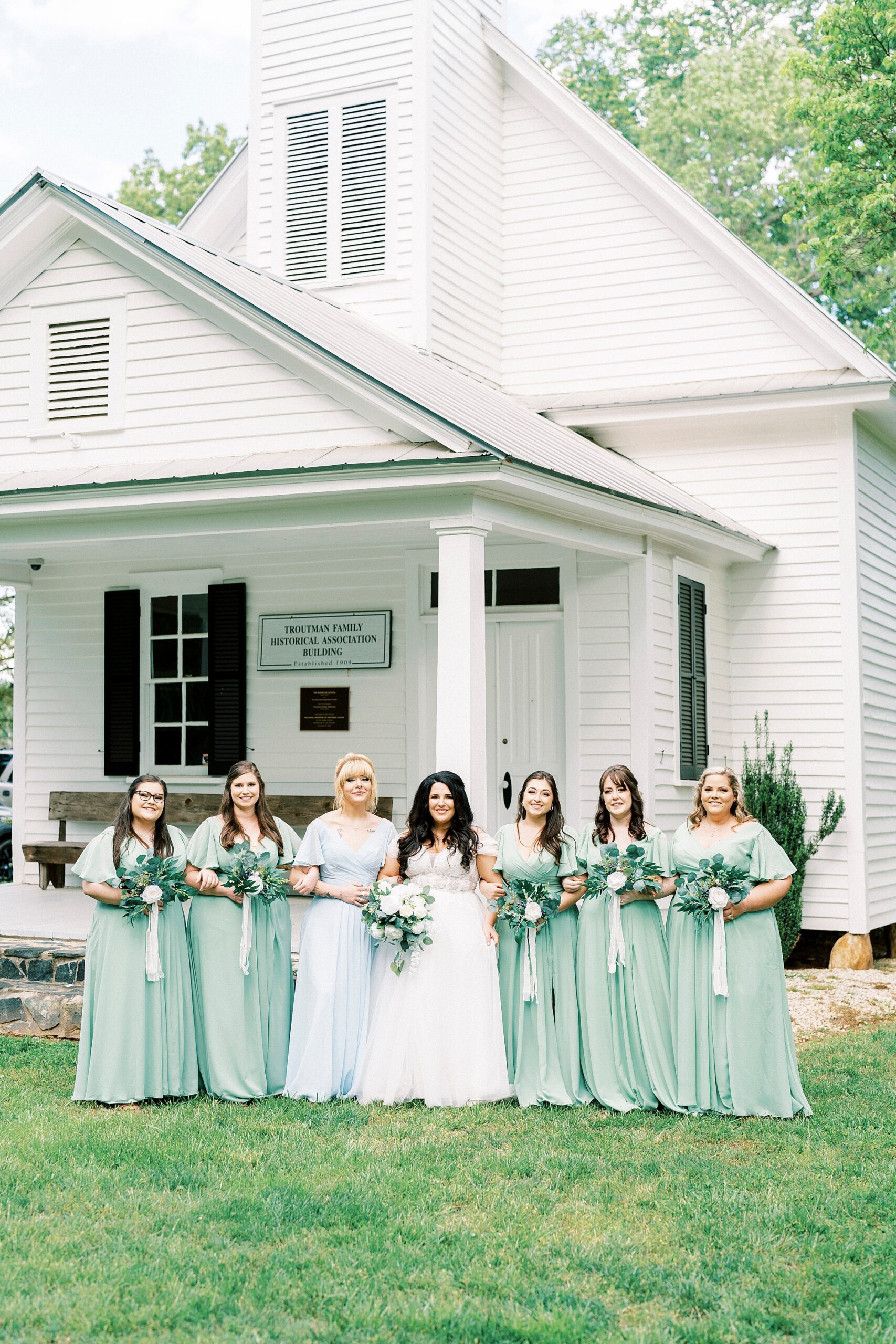 bride walks with bridesmaids in mint gowns outside white chapel 