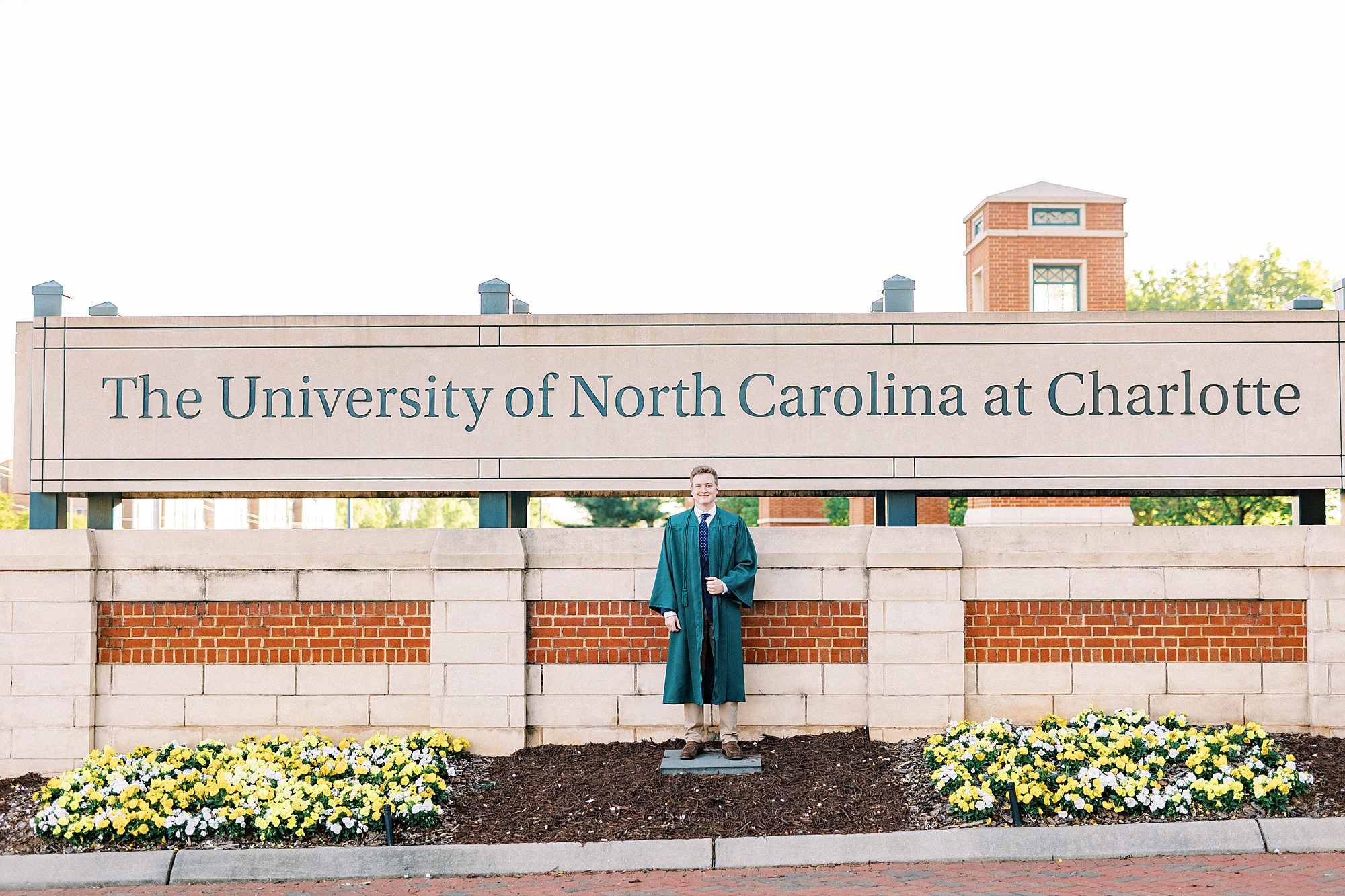 senior poses in green gown by University of North Carolina at Charlotte sign