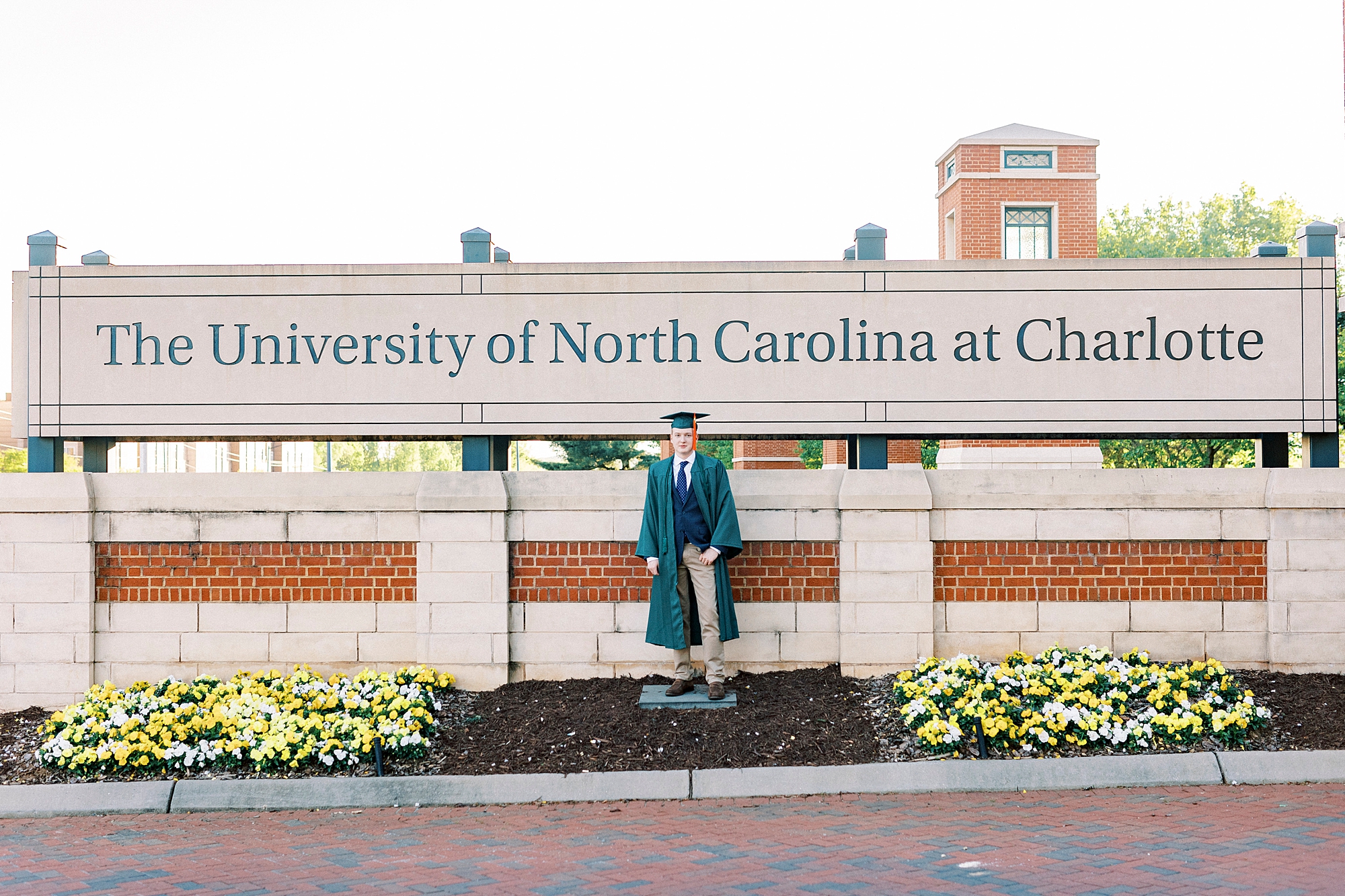 graduating senior leans against University of North Carolina at Charlotte sign