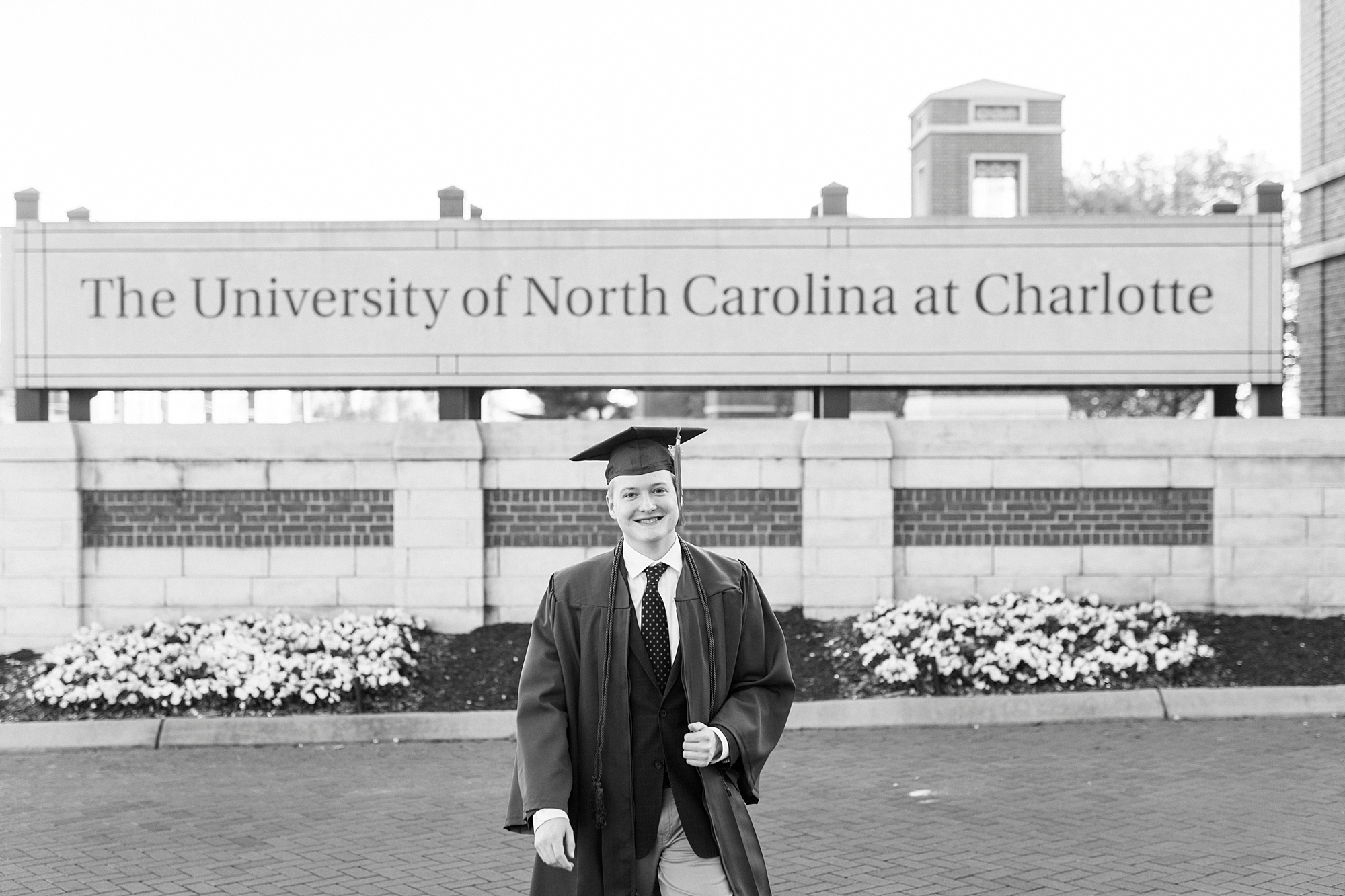 senior stands in cap and gown by University of North Carolina at Charlotte sign