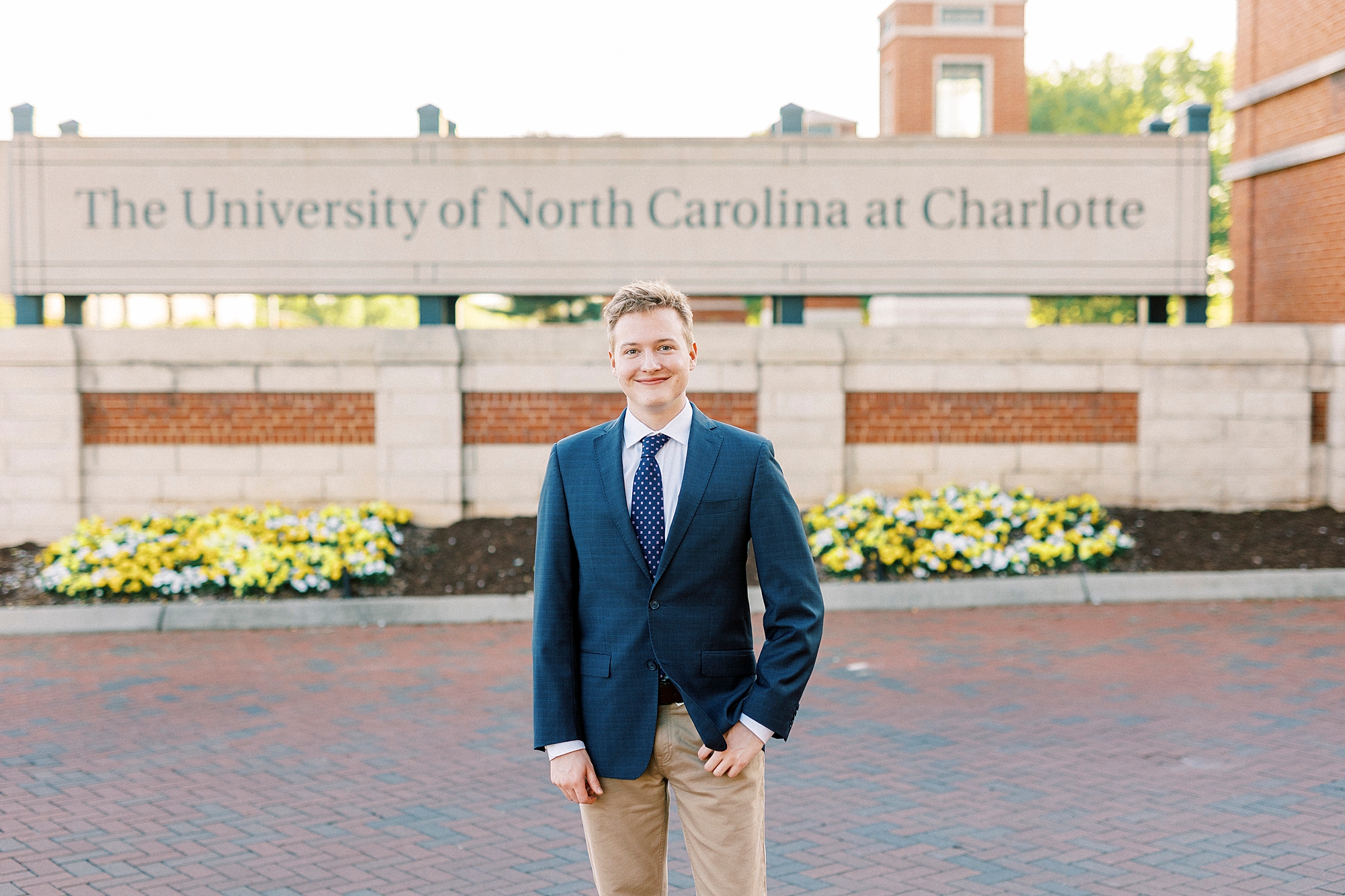 senior in navy jacket with khaki pants stands near University of North Carolina at Charlotte sign