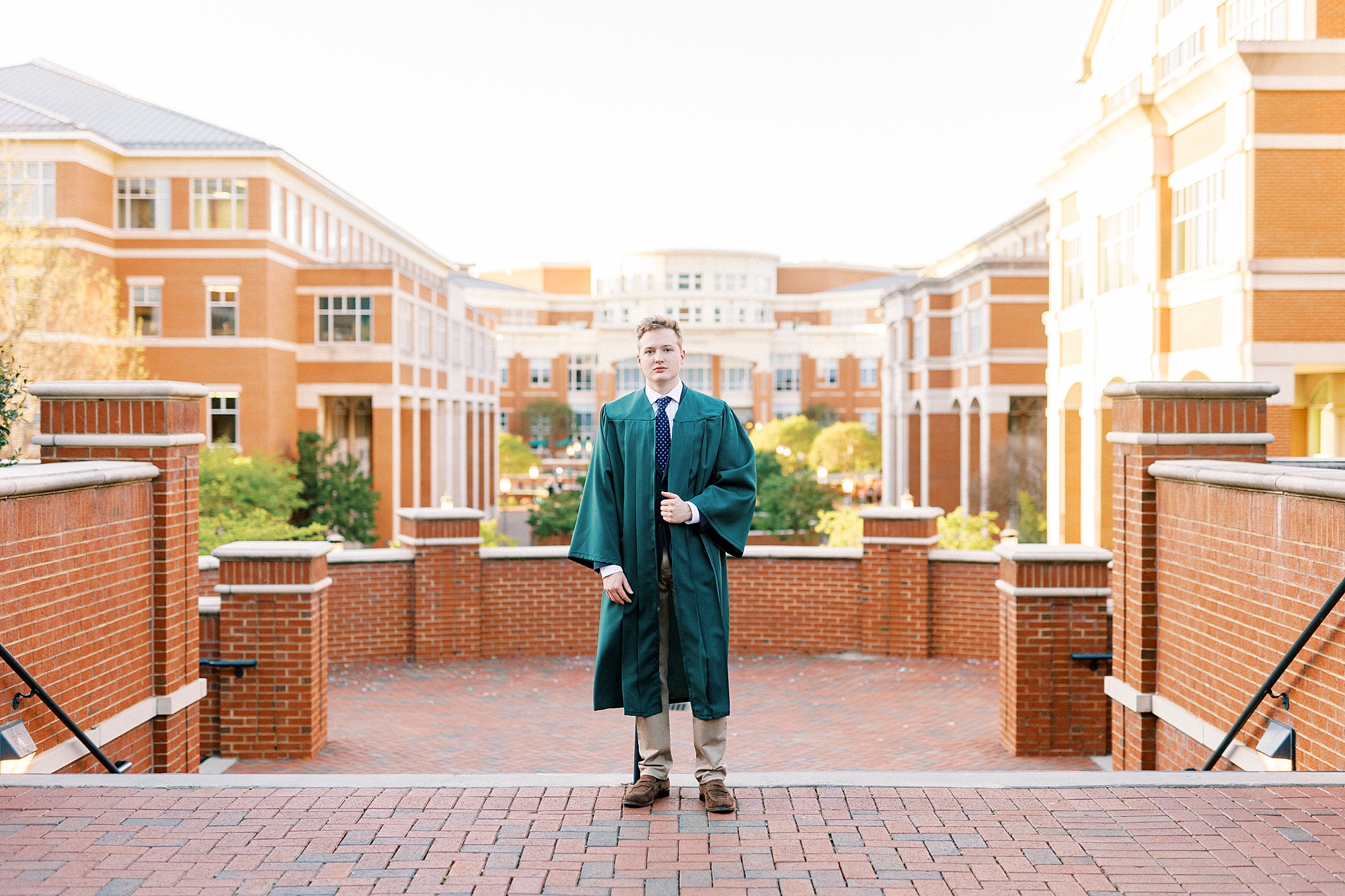 senior guy in green gown stands on quad at UNC Charlotte