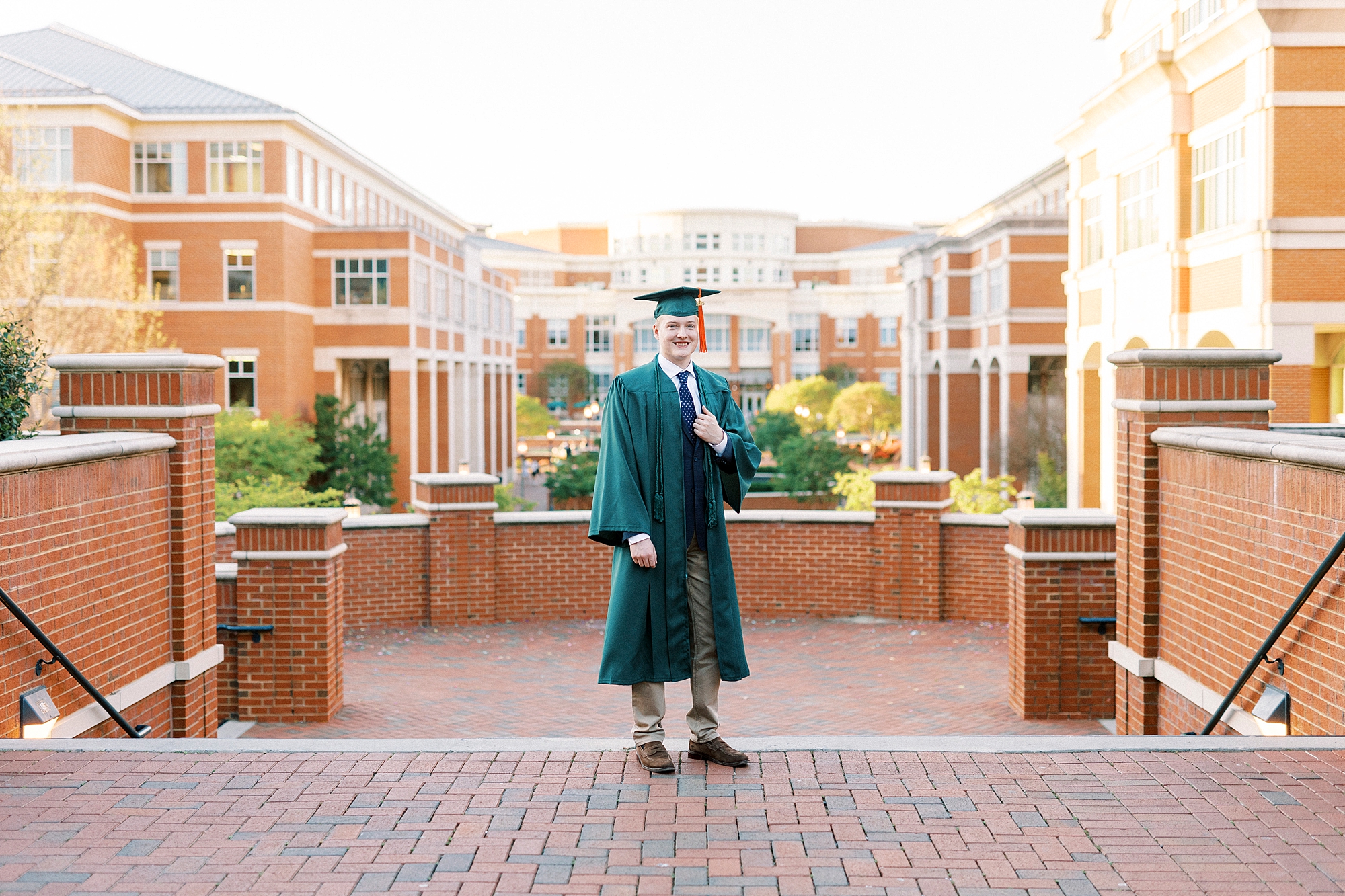 groom stands with hand on lapel of graduation gown in quad at UNC Charlotte