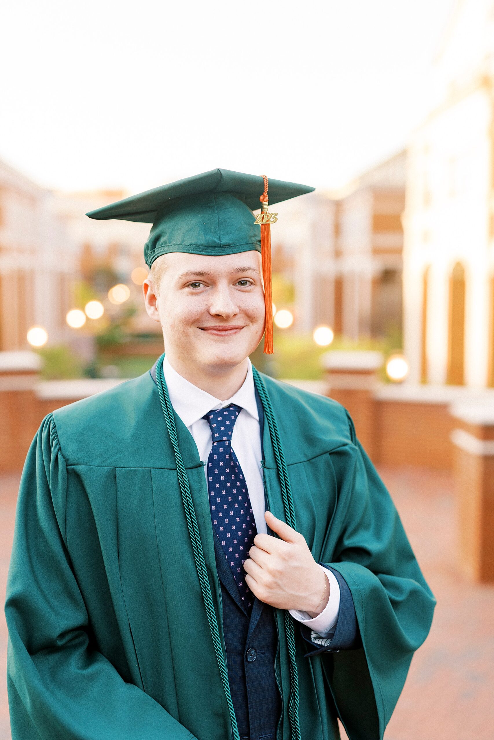 graduating senior poses in green cap and gown during UNC Charlotte senior portraits 