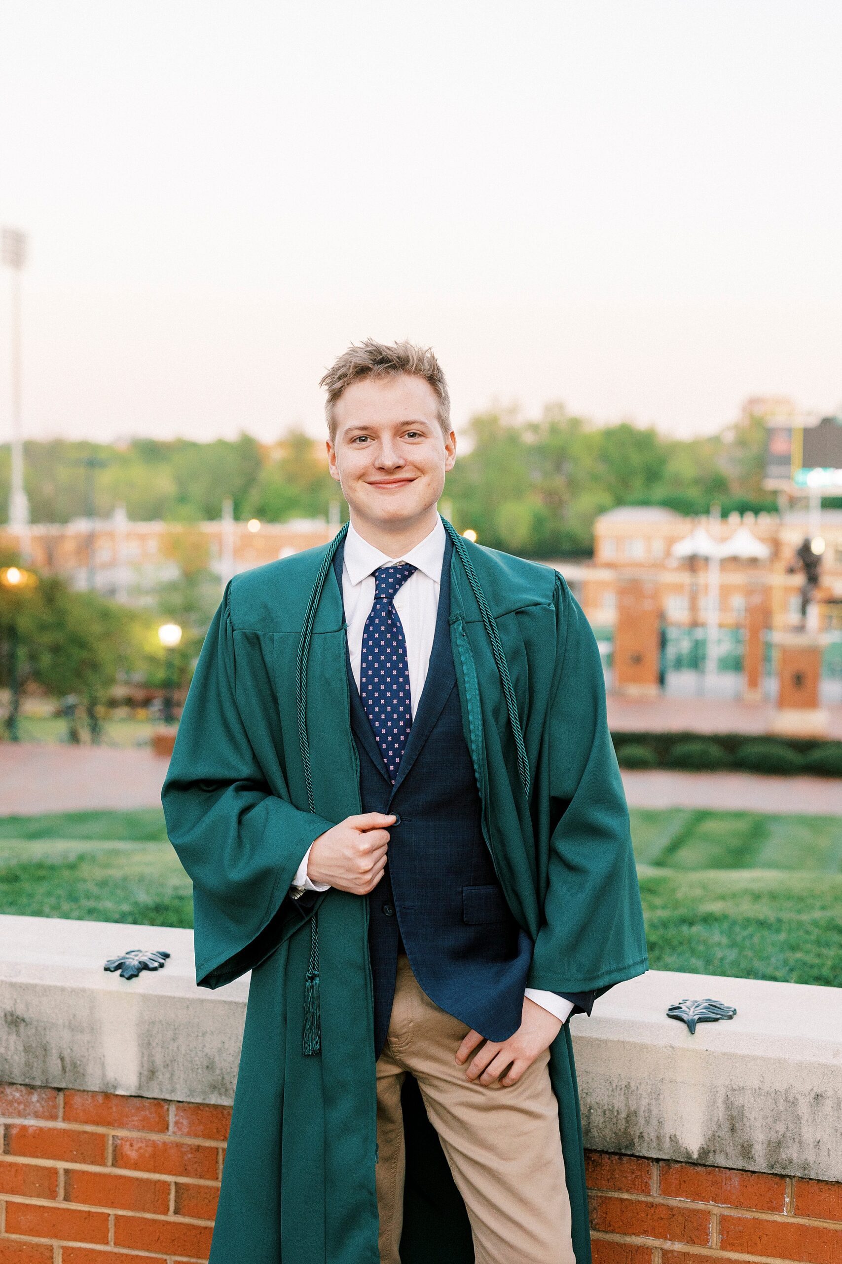 senior stands holding lapel of green graduation gown