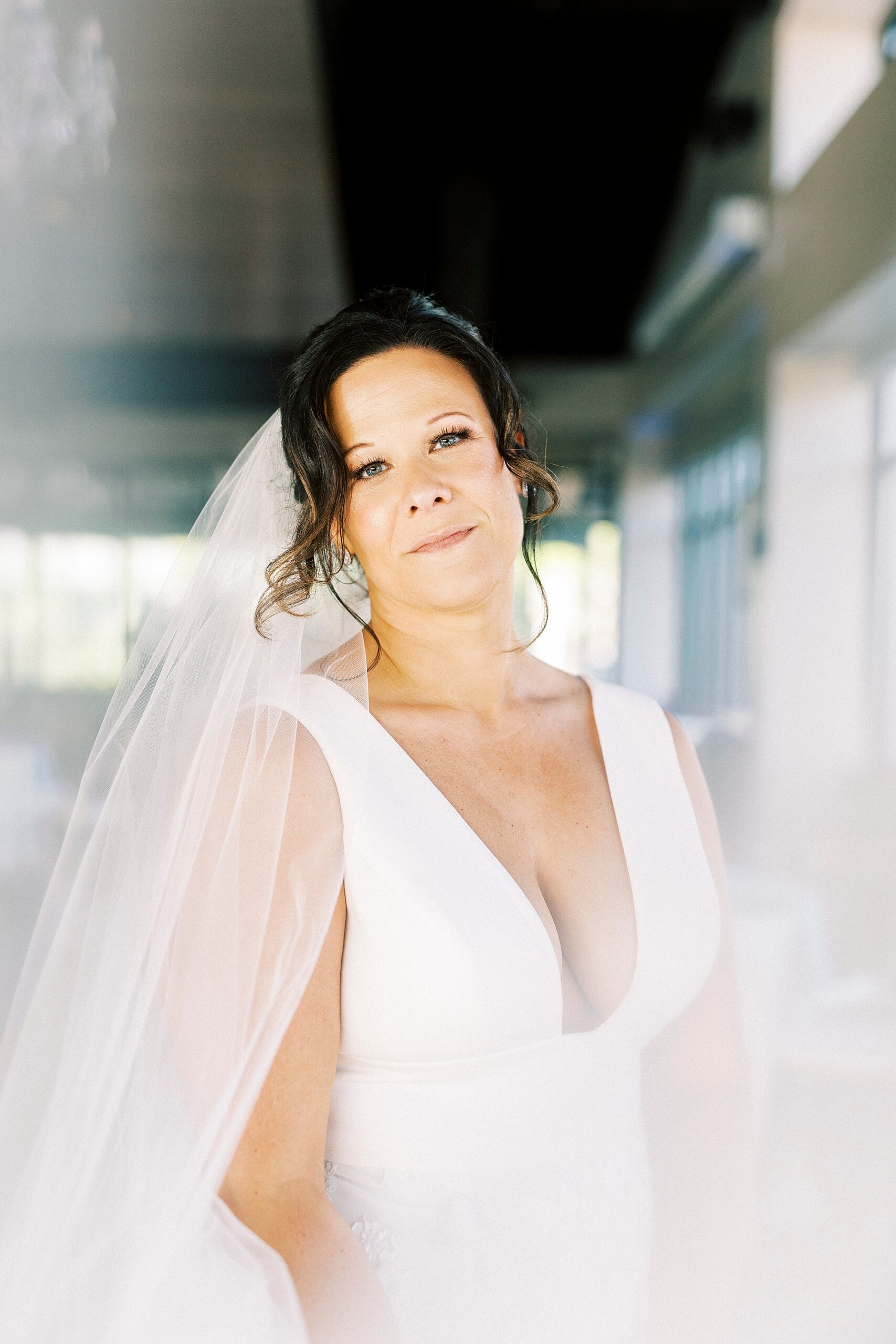 bride smiles leaning head to the side with veil around her shoulders