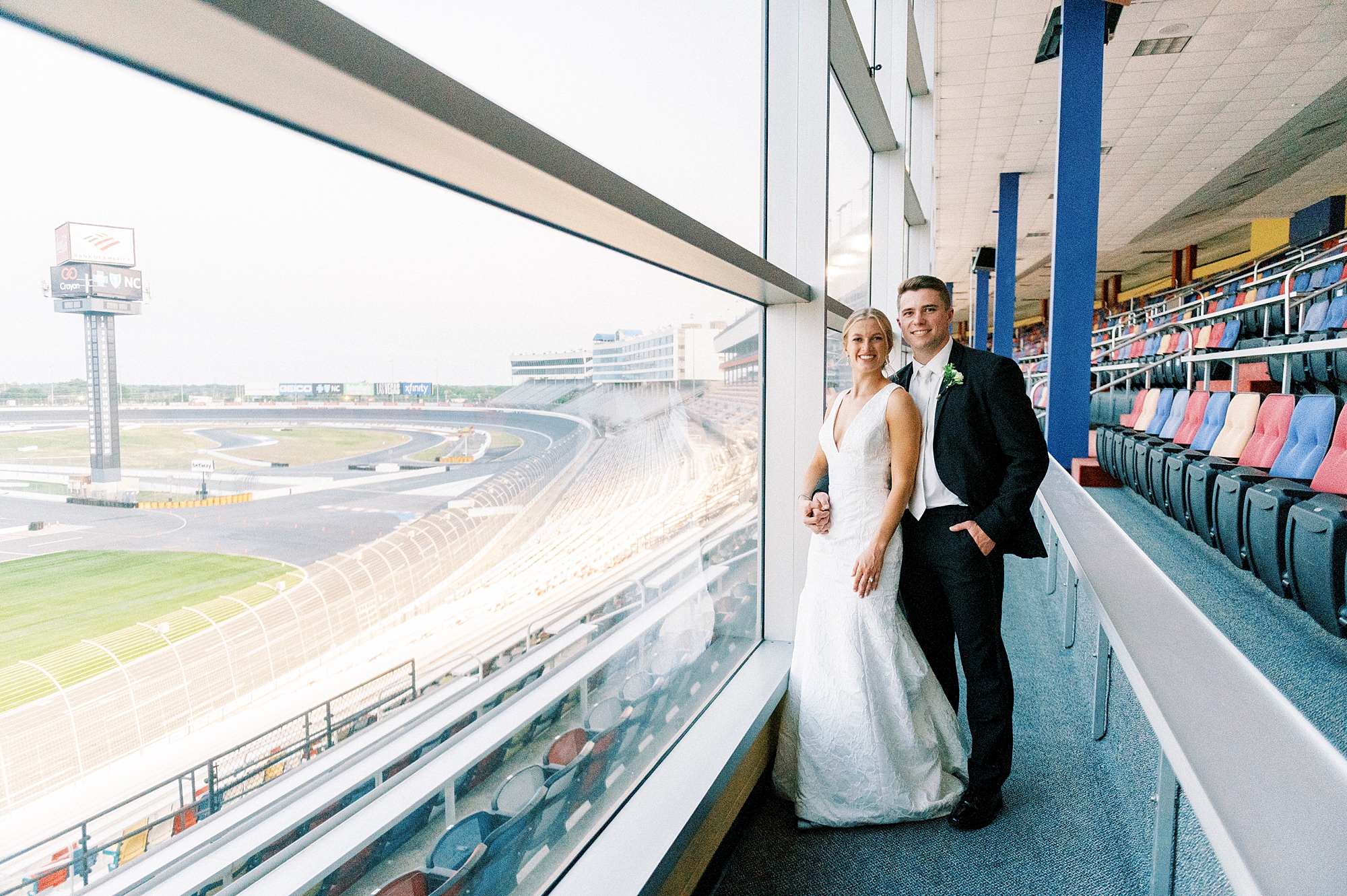 bride and groom hug by glass panel overlooking the Charlotte Motor Speedway