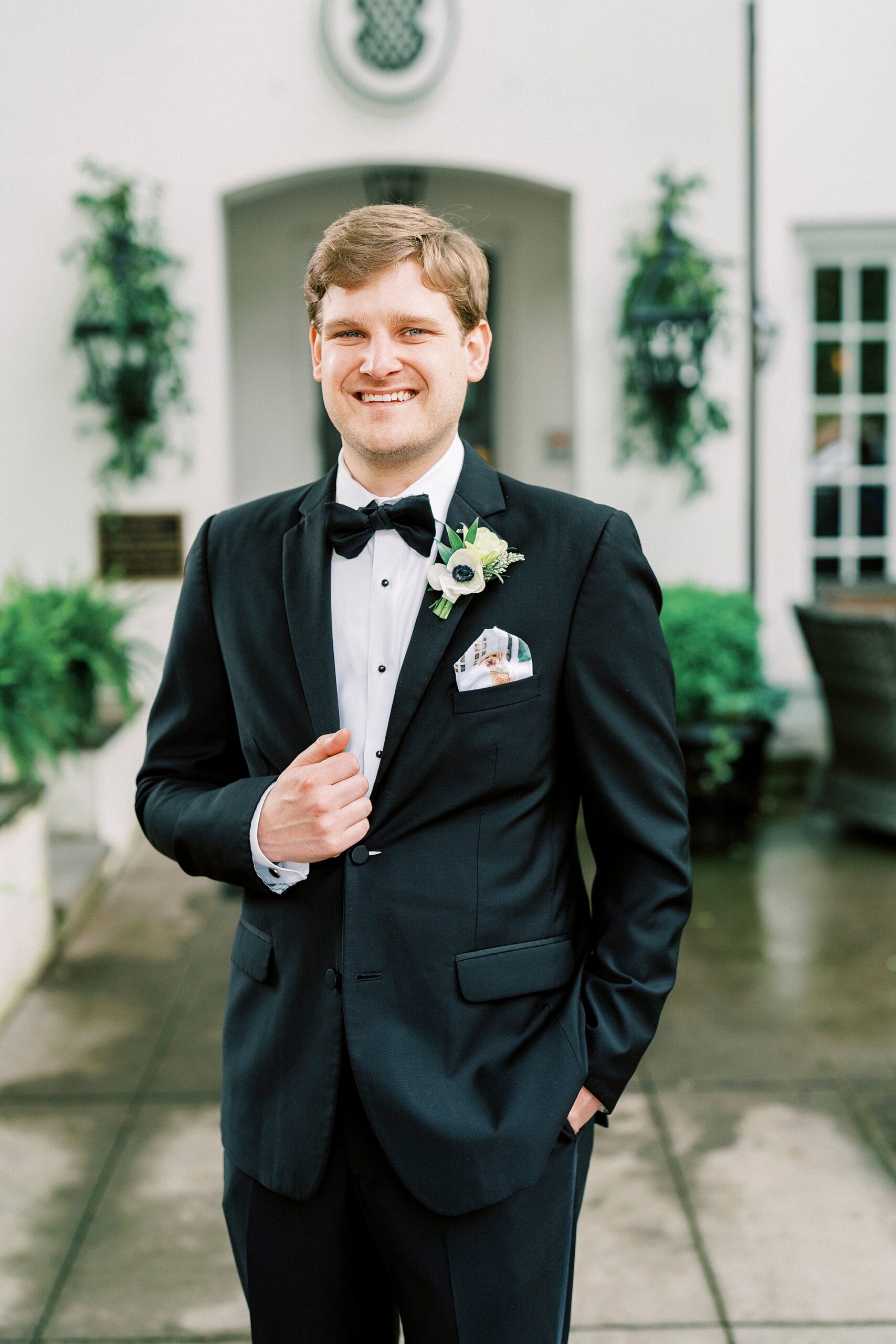 groom stands holding lapel of black suit outside The Spring House