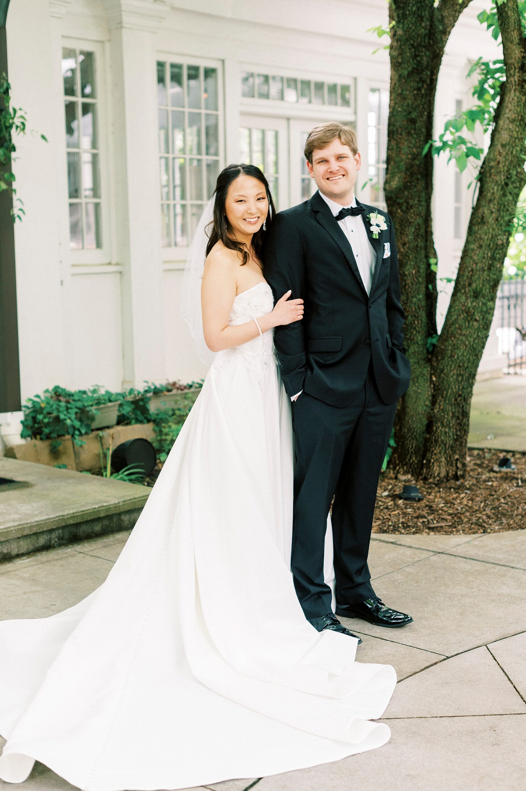 bride stands behind groom holding his arm outside The Spring House