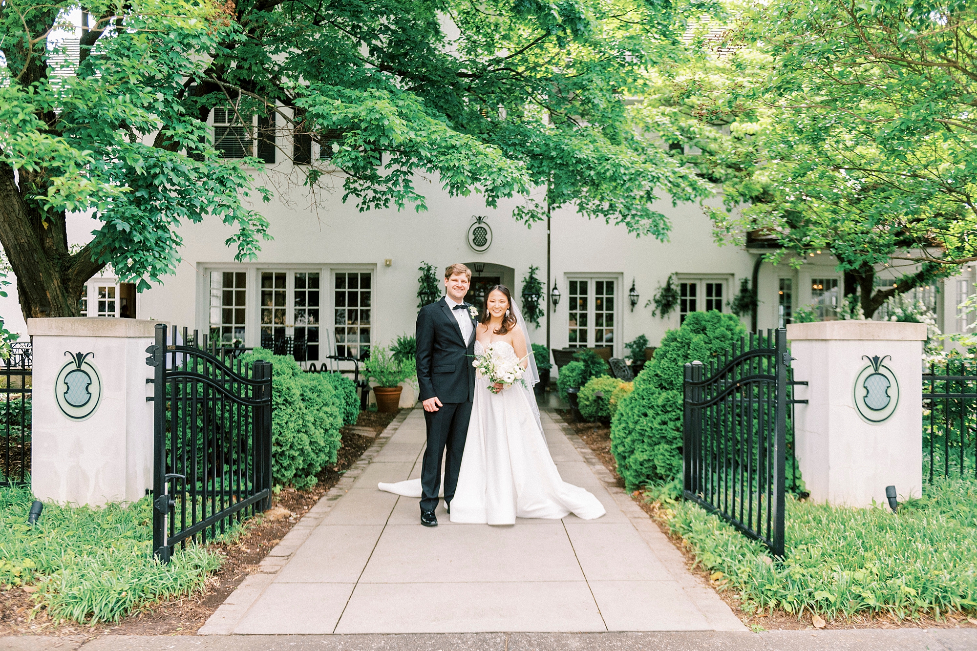 bride and groom stand outside The Spring House on pathway in gardens