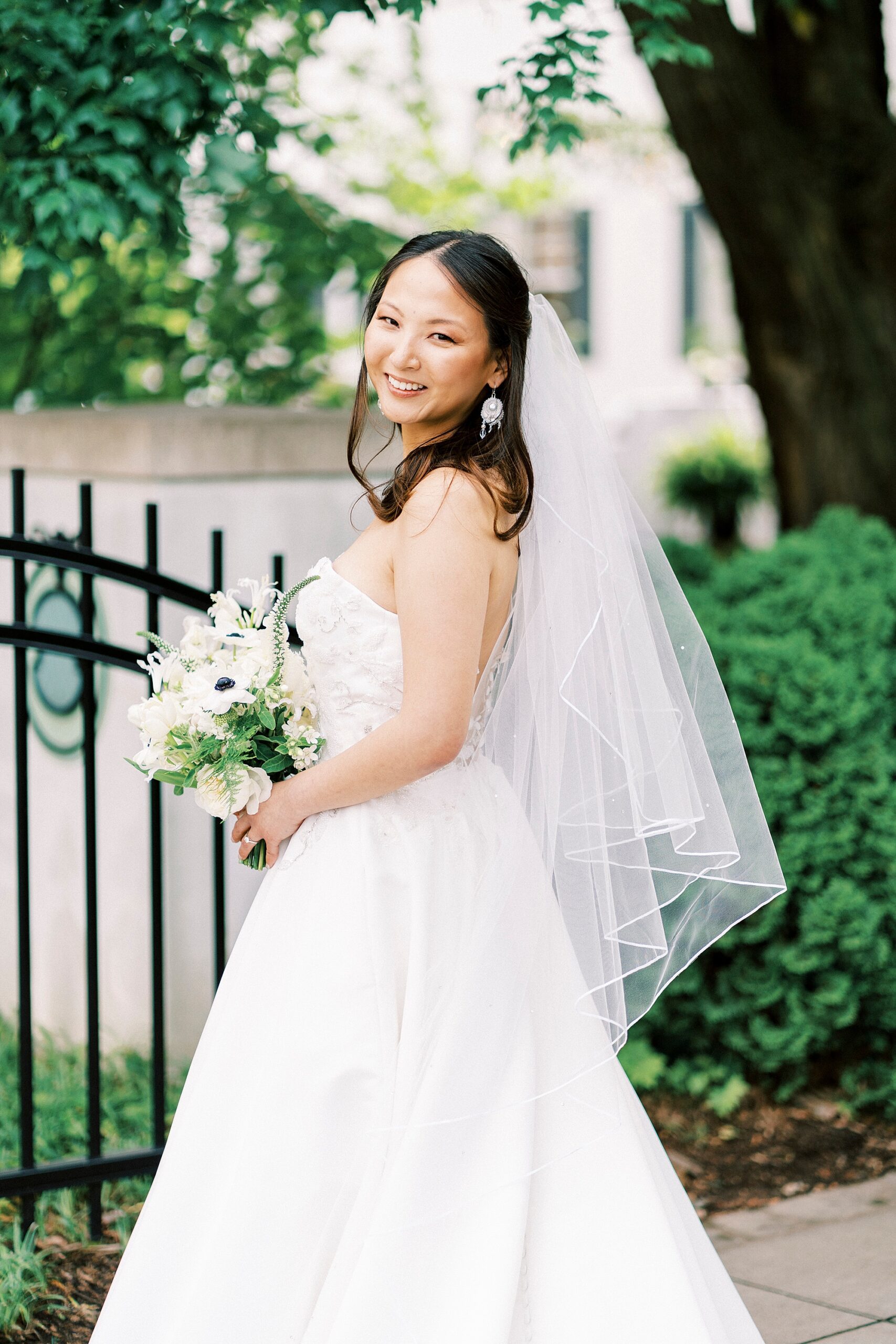 bride smiles looking over shoulder with veil behind her by wrought iron gate