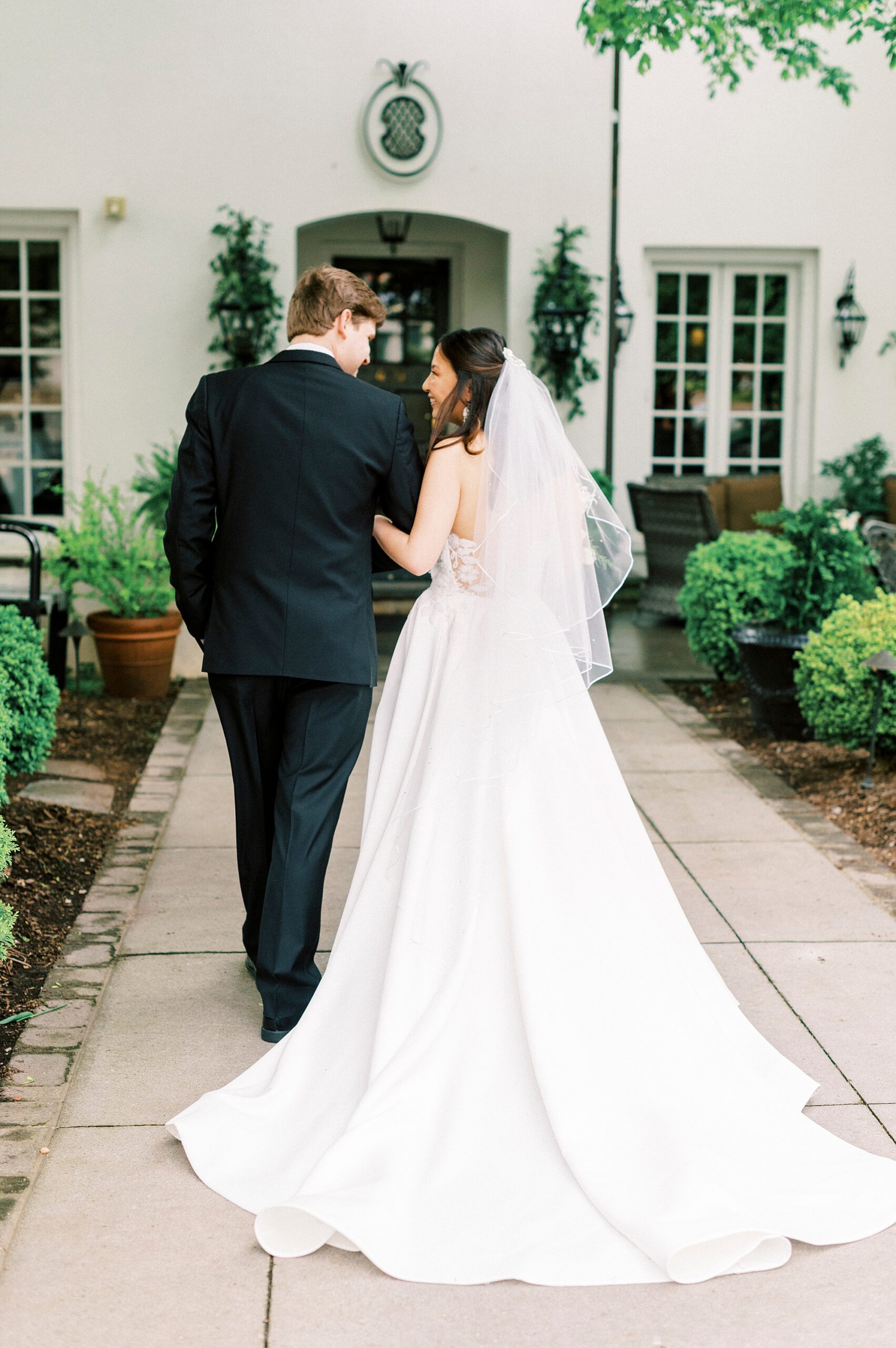 bride holds groom's arm walking down pathway outisd eThe Spring House