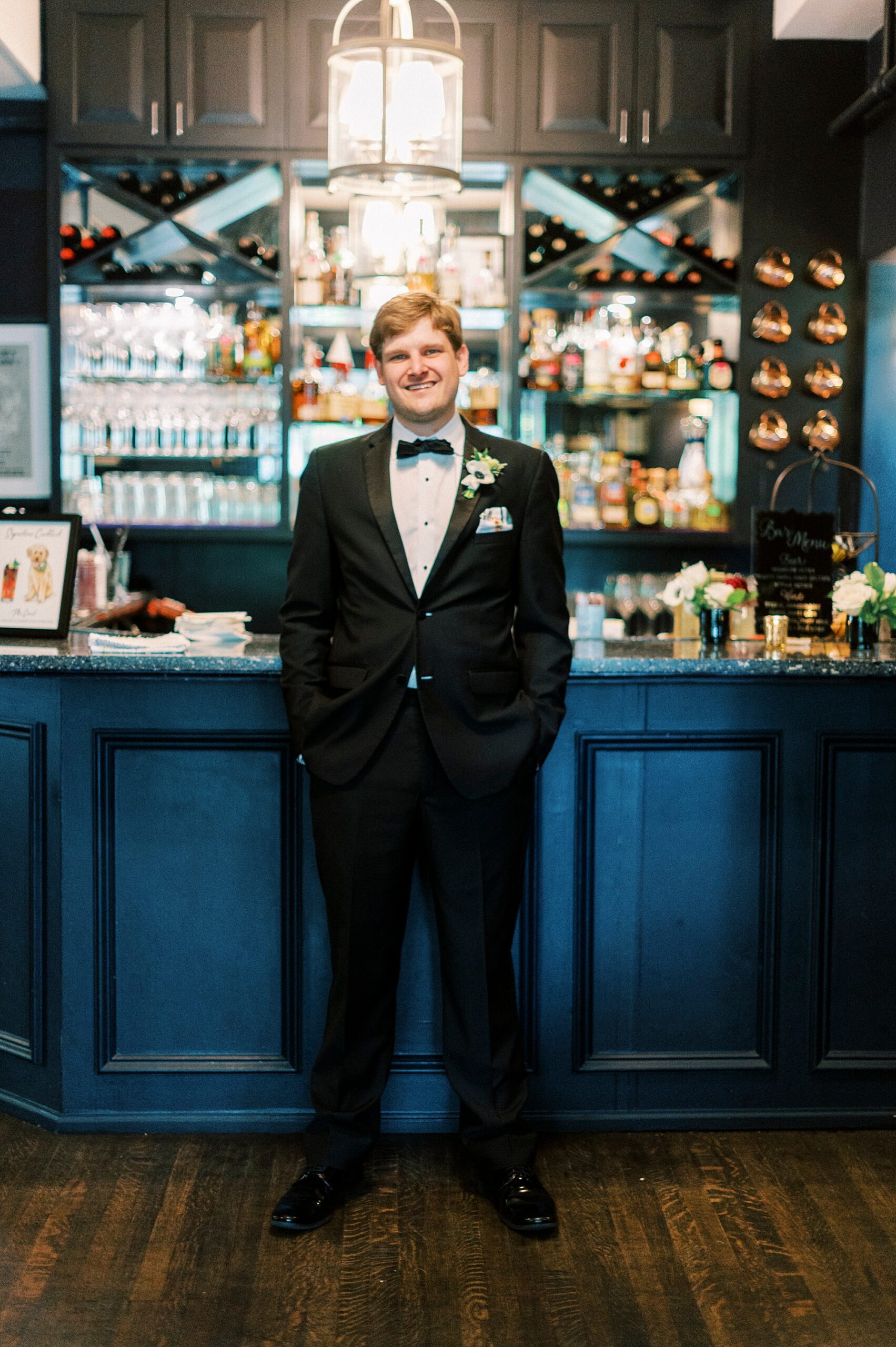 groom stands in front of bar with blue walls at The Spring House