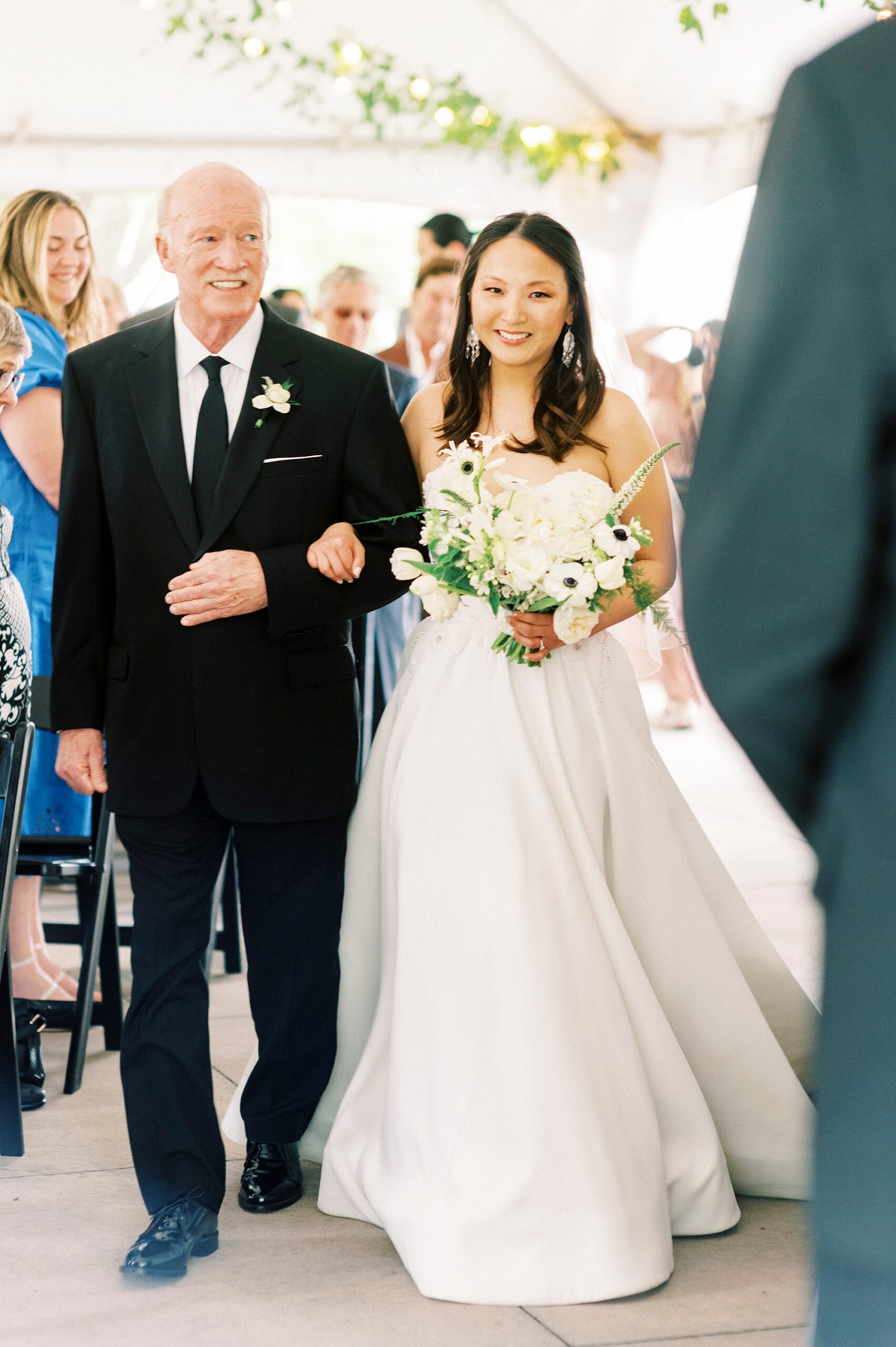 bride walks down aisle with father holding bouquet of ivory flowers