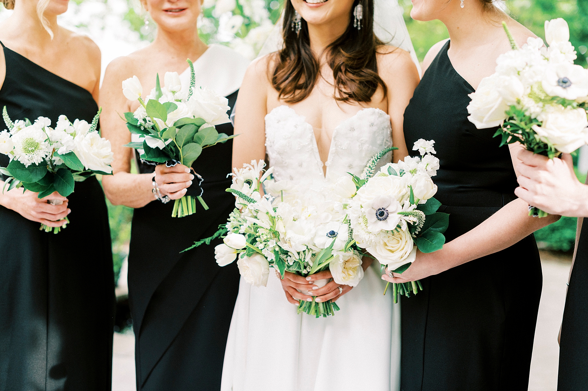bride stands with bridesmaids in black dresses with white bouquets 