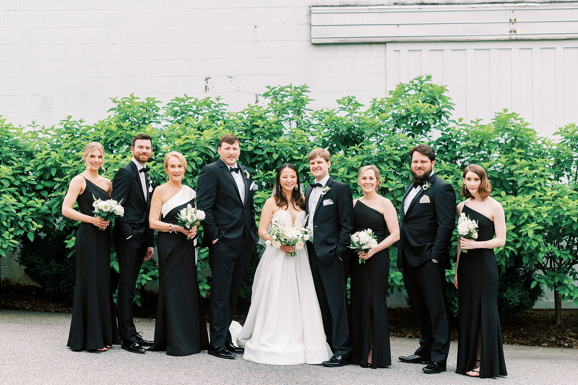 bride and groom stand with wedding party in black dresses and suits
