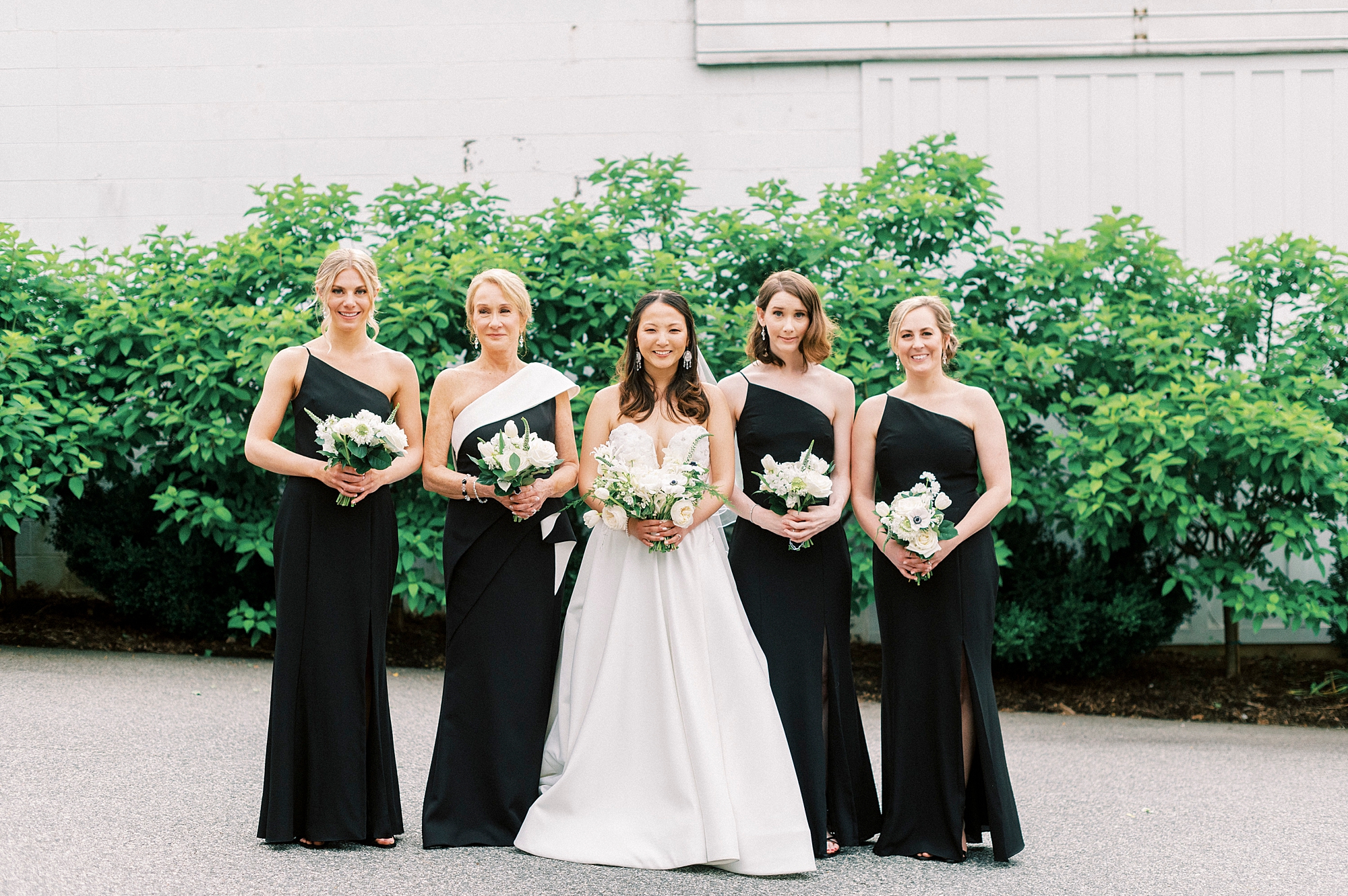bride stands with bridesmaids in one-shoulder black dresses 
