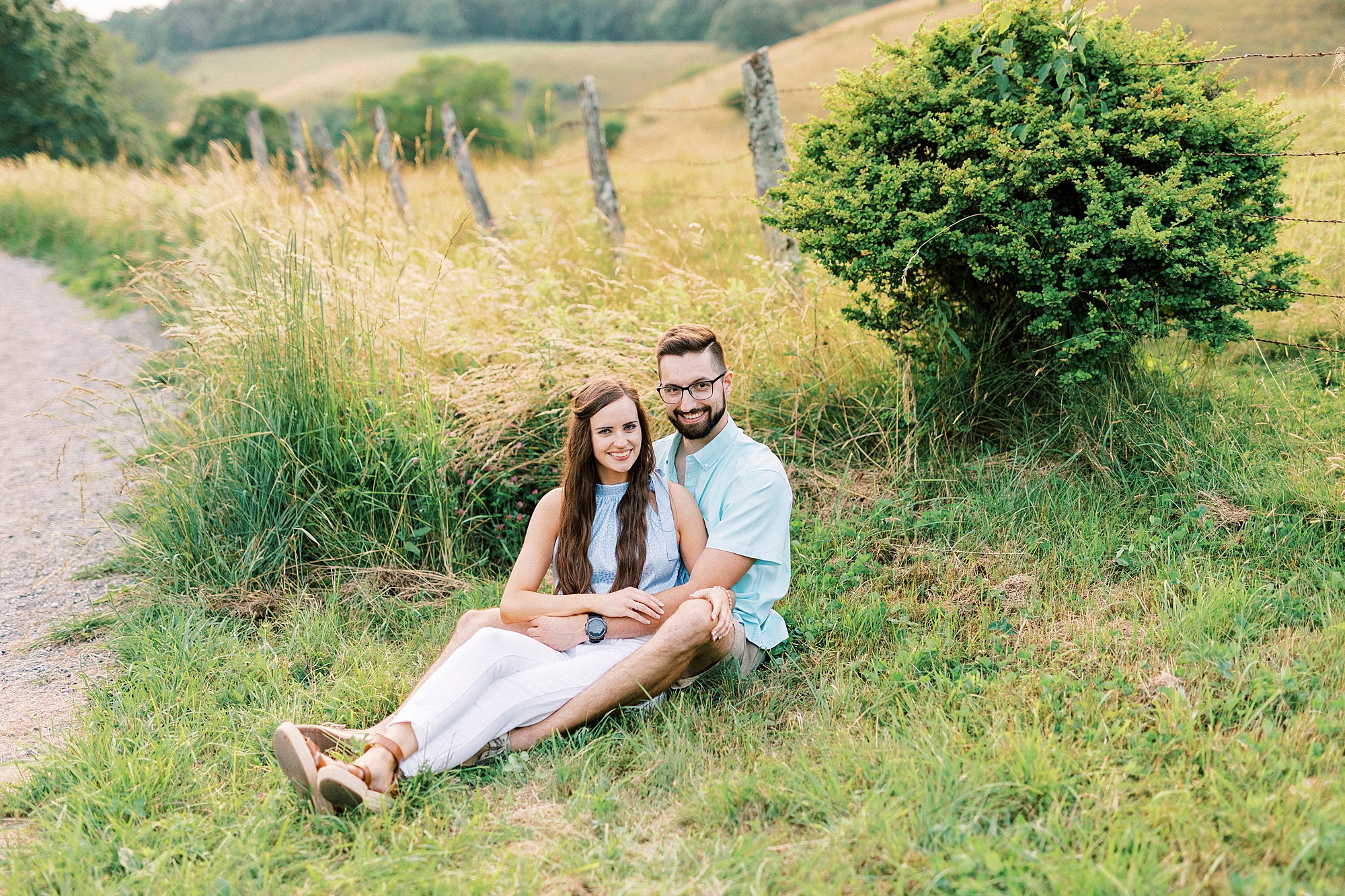 couple sits together in field on hill at Moses Cone Manor