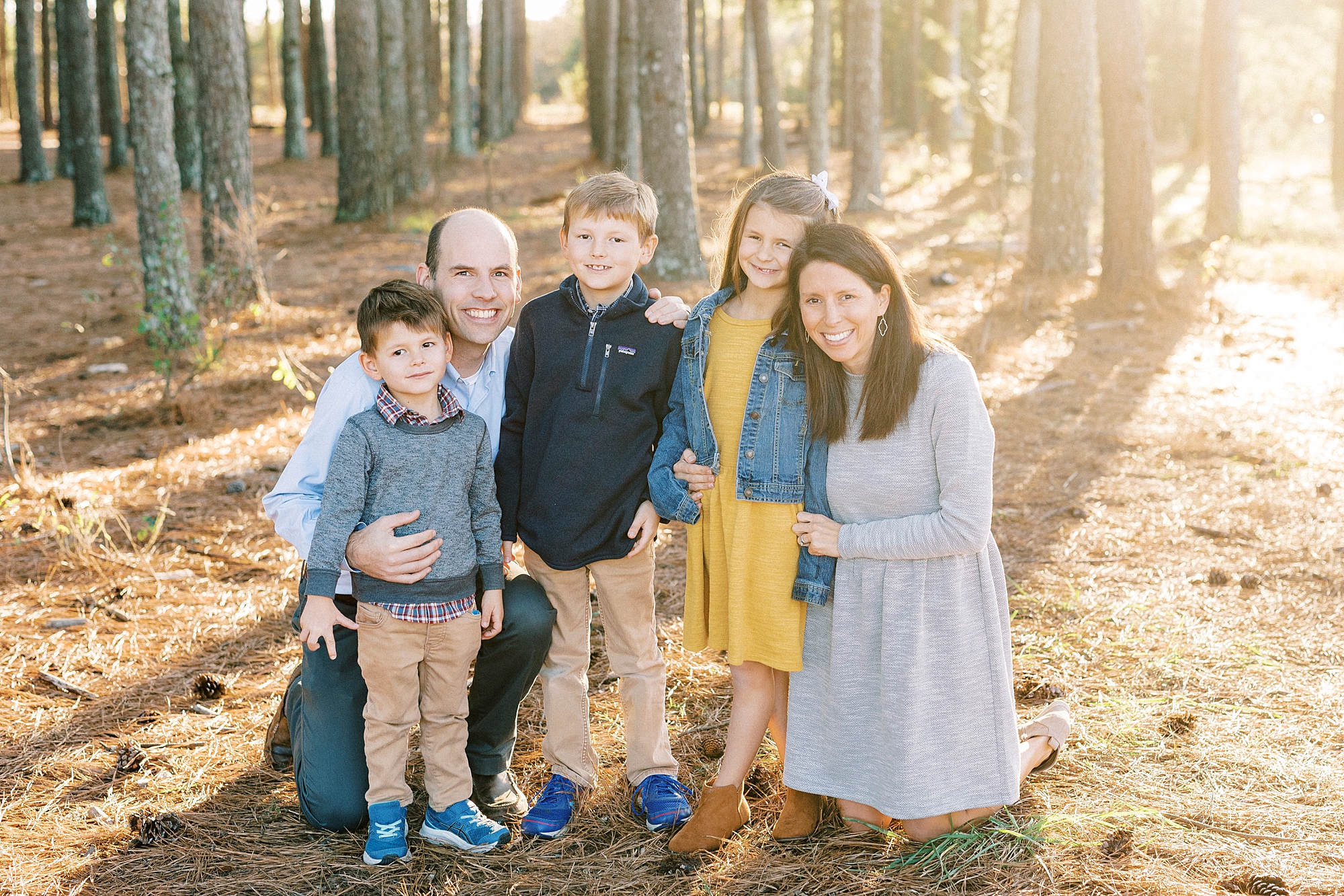 mom and dad kneel with three children during family photos in the fall