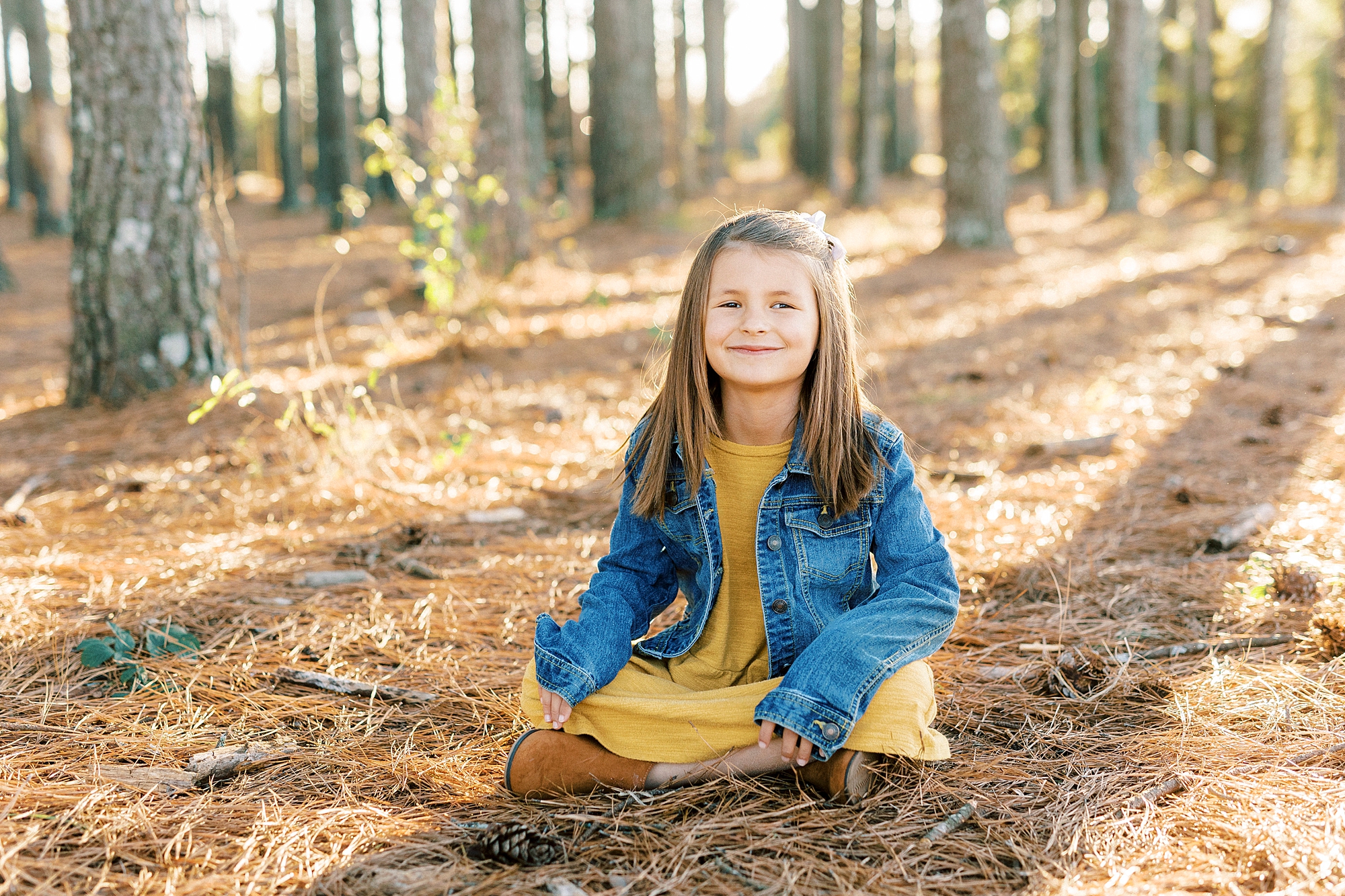girl in yellow dress with jean jacket sits in fallen pine needles at Frank Liske Park
