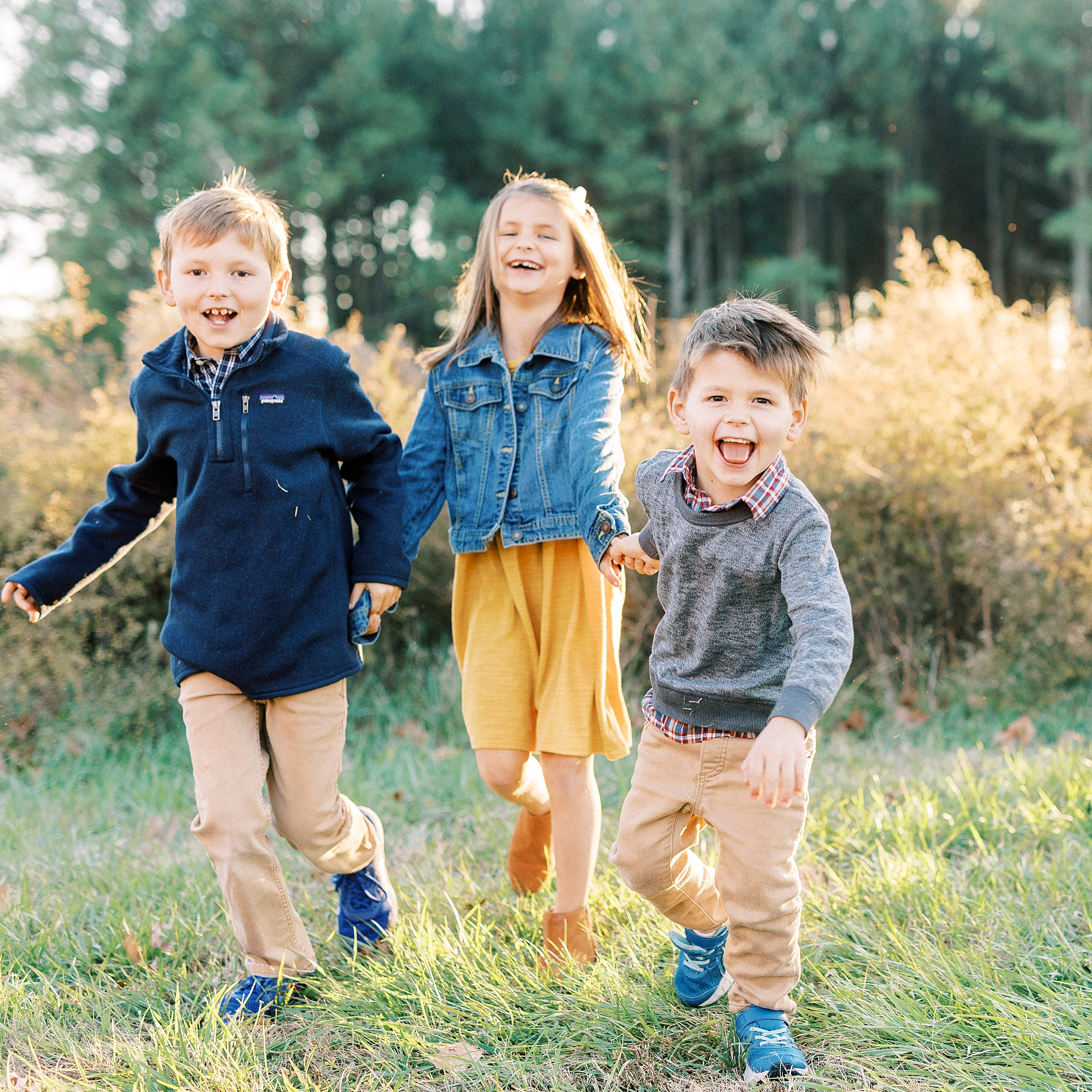three kids laugh and smile running in grass during NC family photos