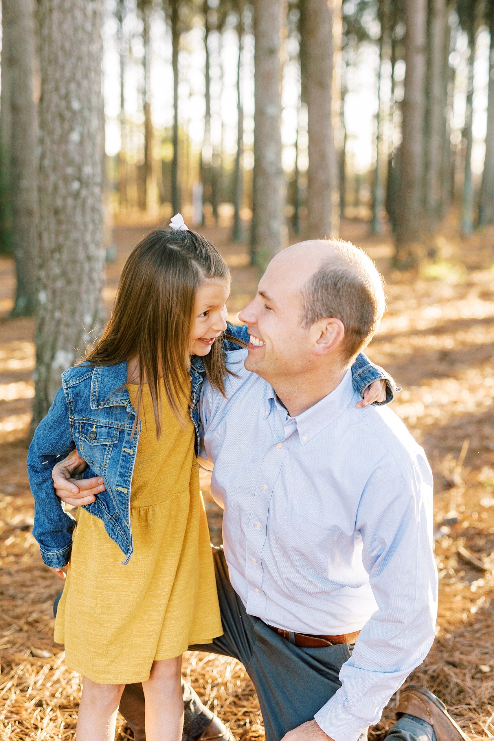 daughter hugs dad around his neck smiling in woods
