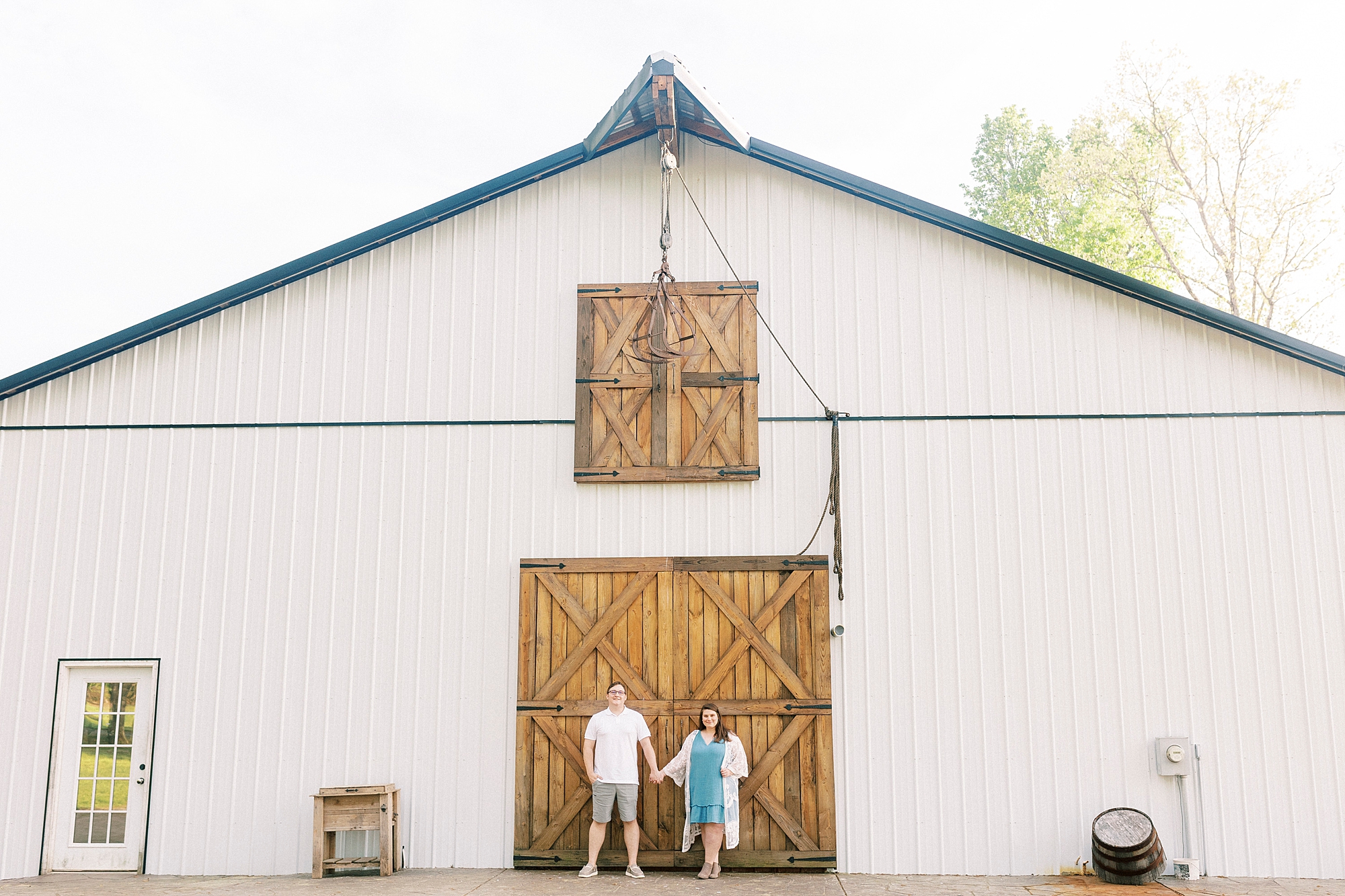 engaged couple holds hands standing in front of wooden doors at the Farmstead
