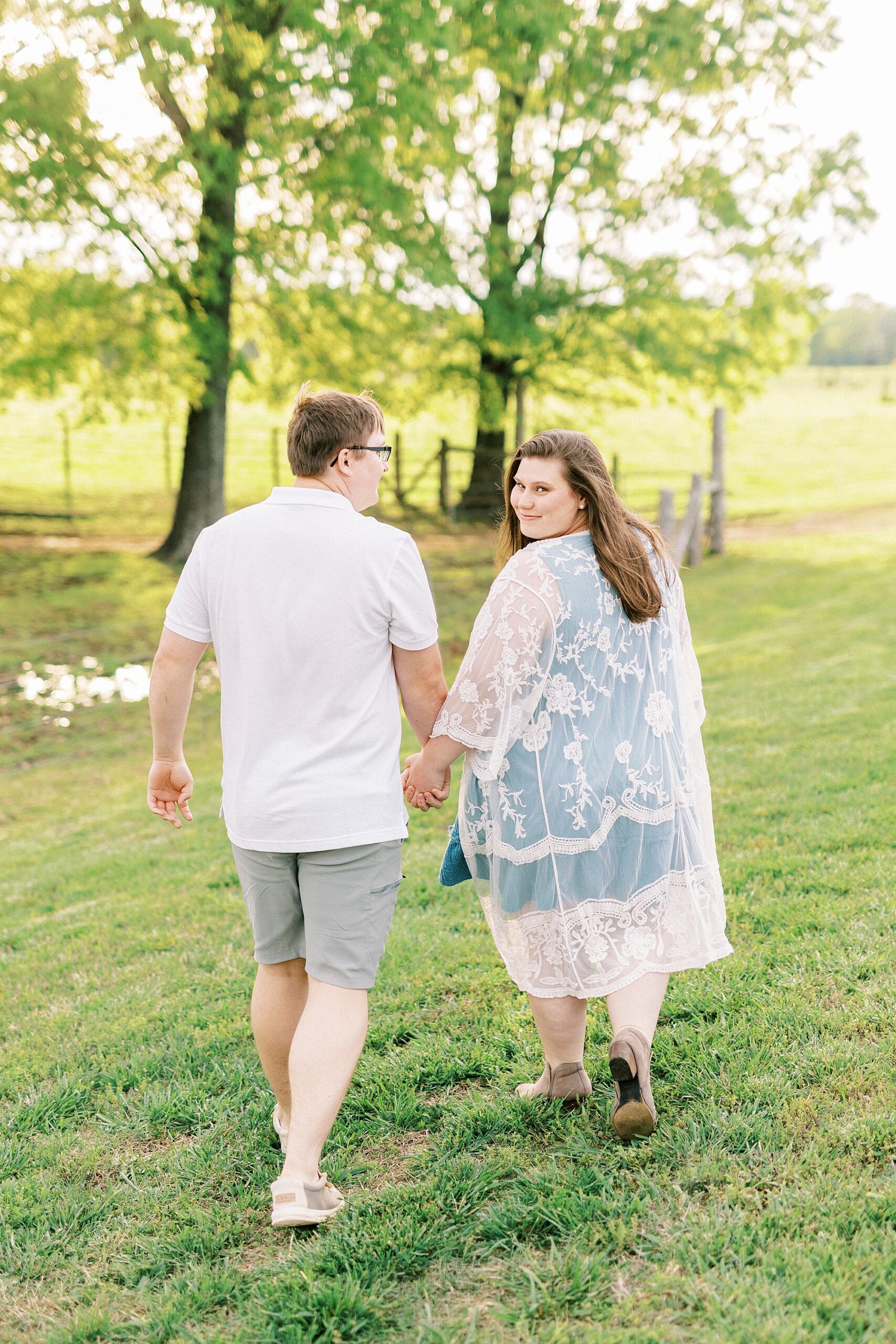 woman in blue dress with white wrap looks over shoulder walking with man across lawn