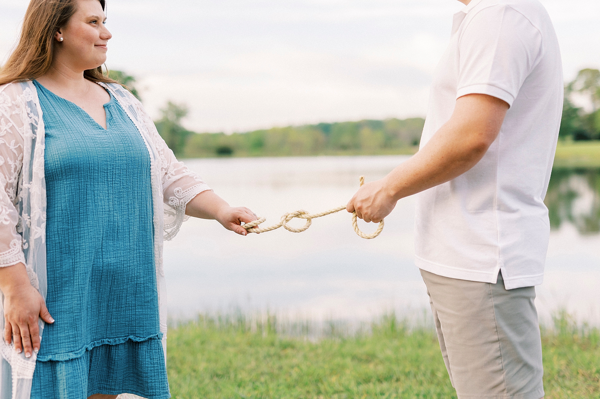 engaged couple holds side of rope near lake at the Farmstead