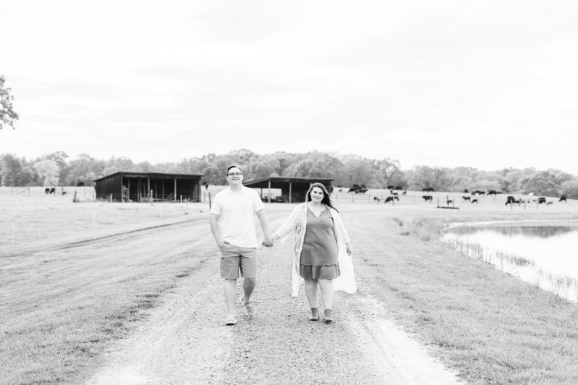 engaged couple holds hands walking down path during summer engagement session at the Farmstead