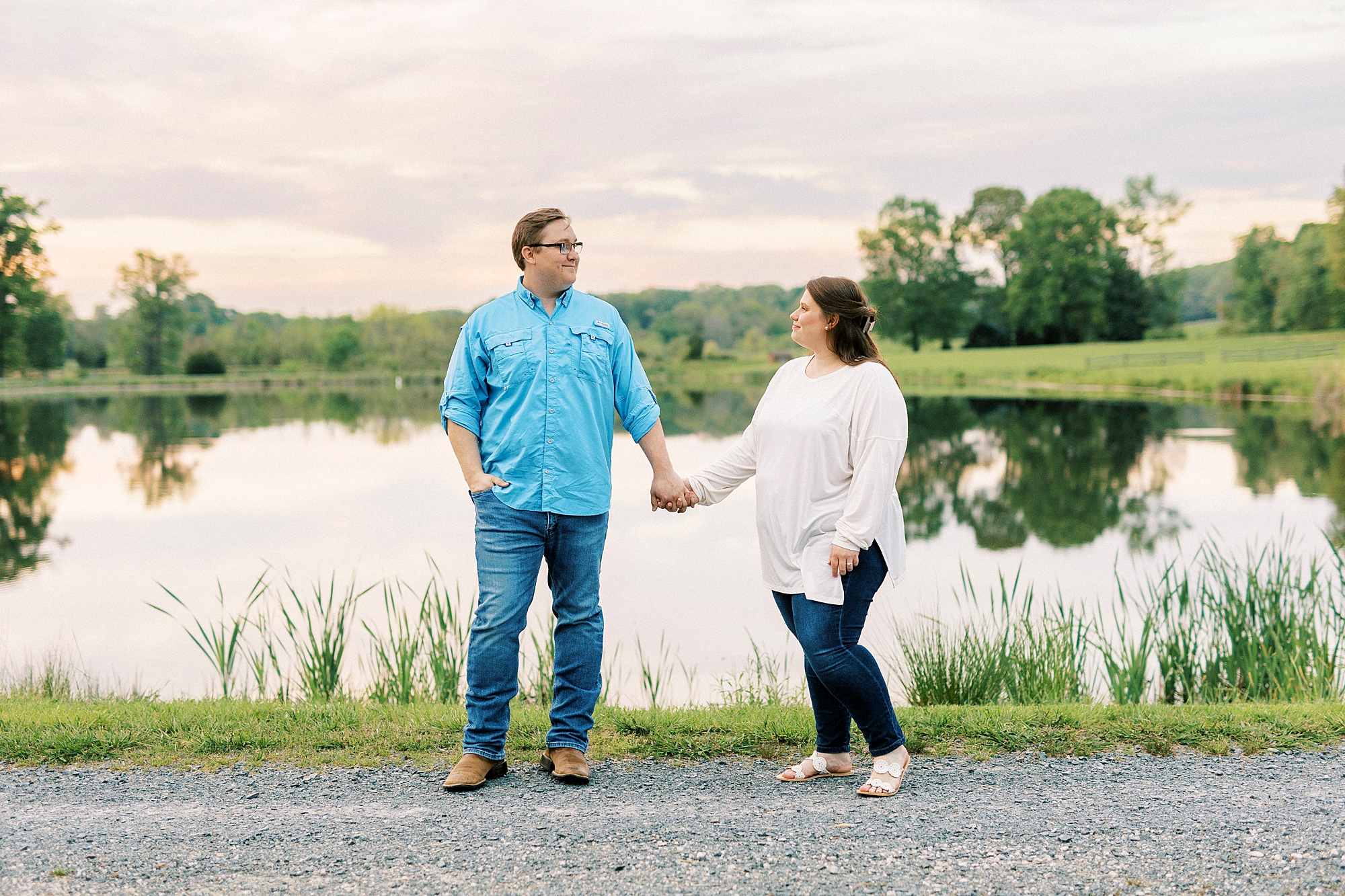 engaged couple holds hands in front of lake at sunset at the Farmstead