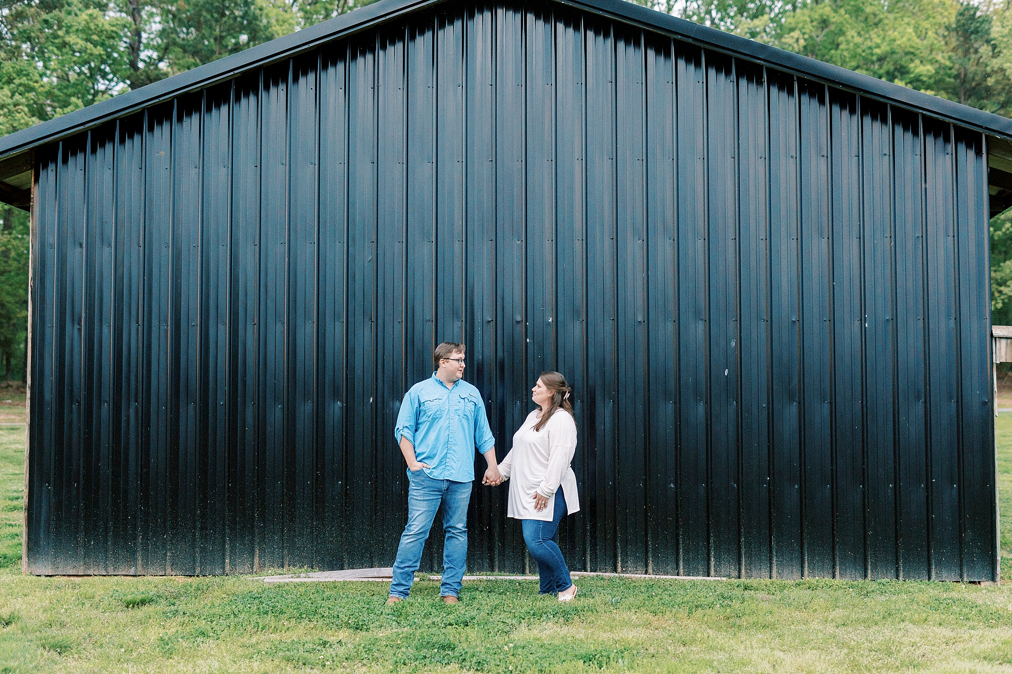 couple holds hands in front of metal barn at the Farmstead