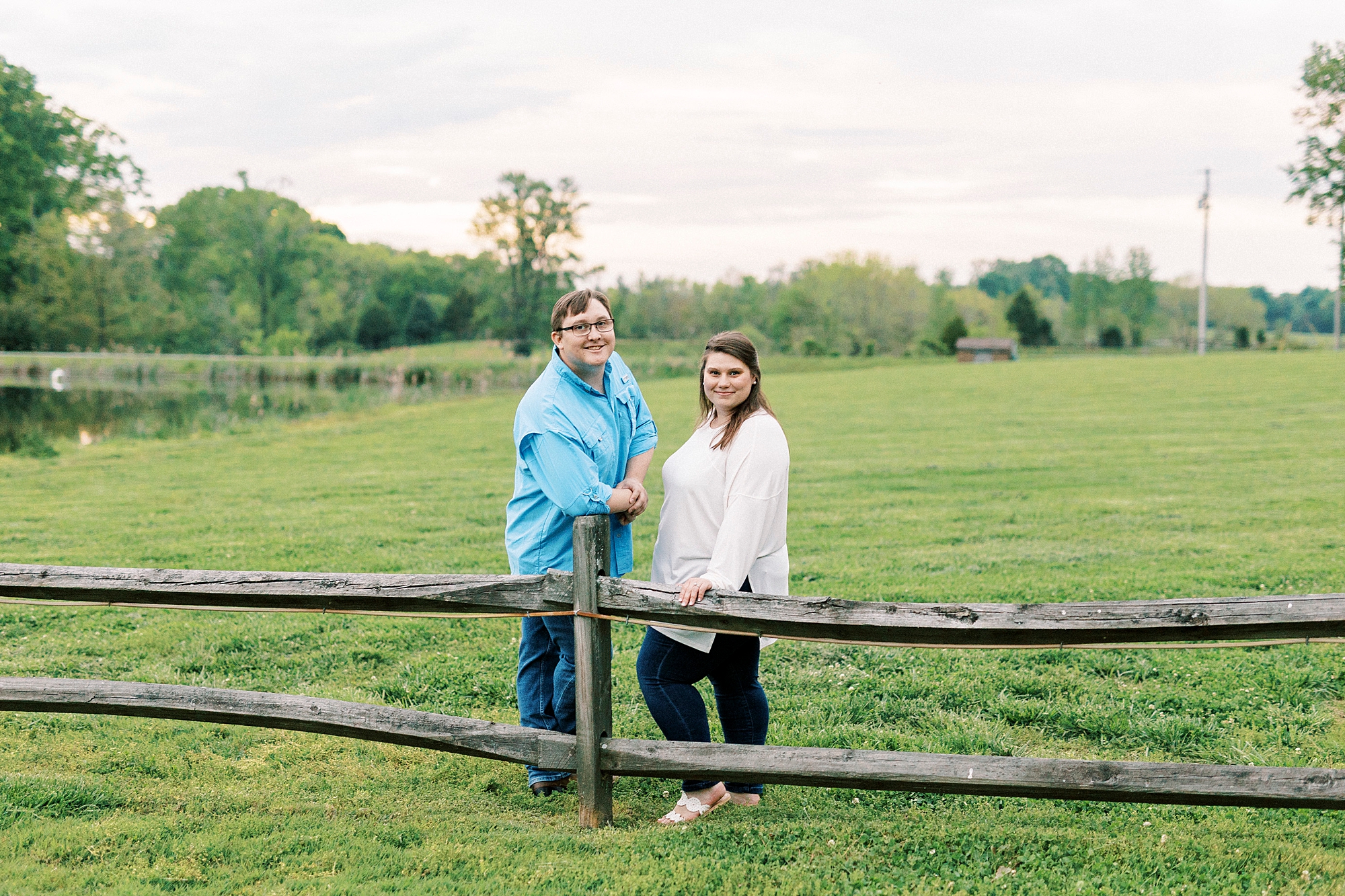 man and woman lean on wooden fence in field at the Farmstead