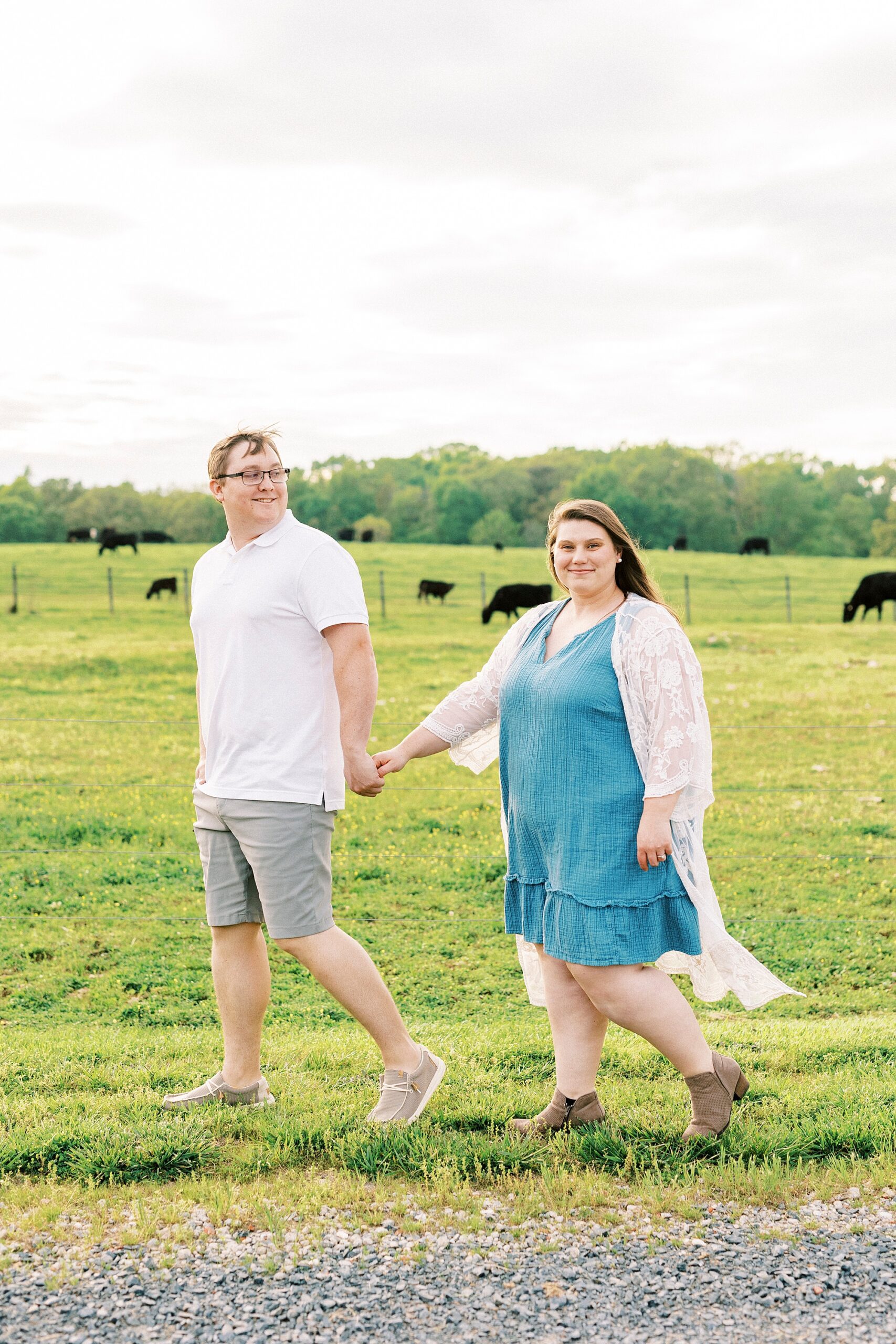 man holds woman's hand walking by cows in field at the Farmstead