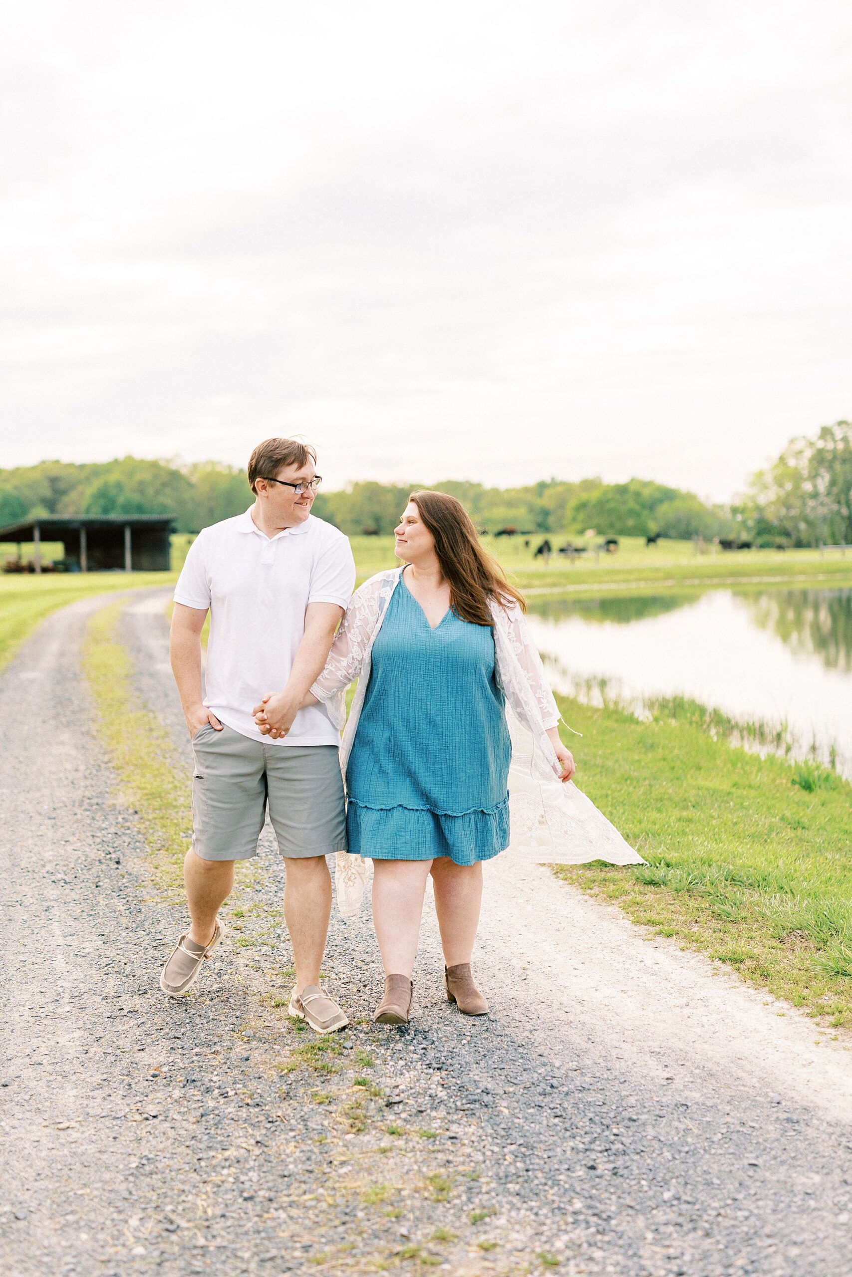 engaged couple holds hands walking on path at the Farmstead
