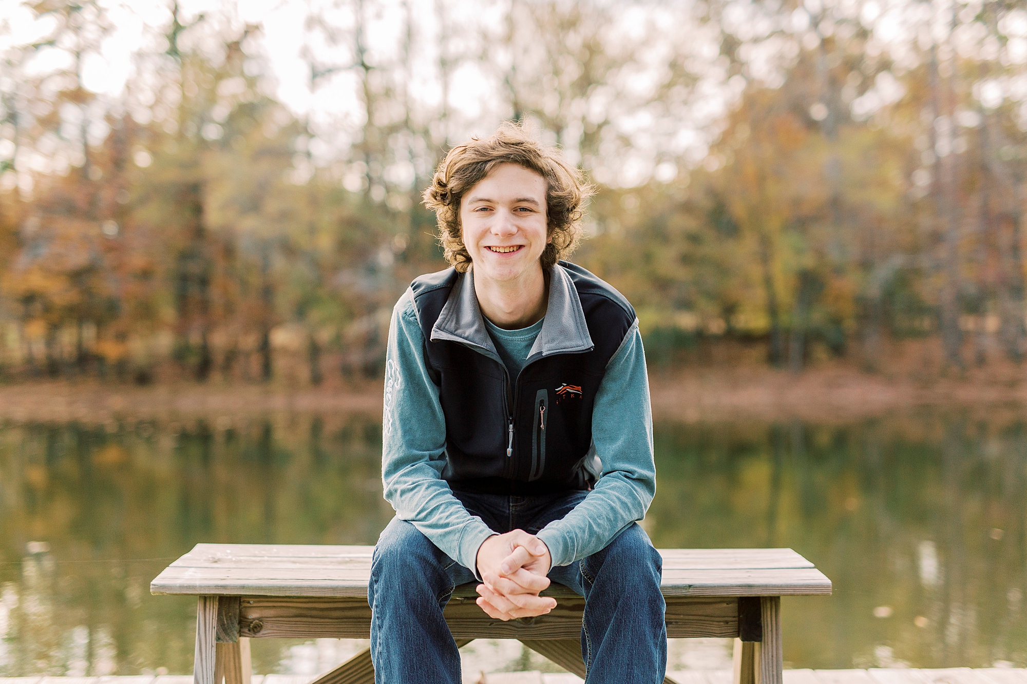 boy sits on bench leaning on knees during fall Midland NC senior portraits 