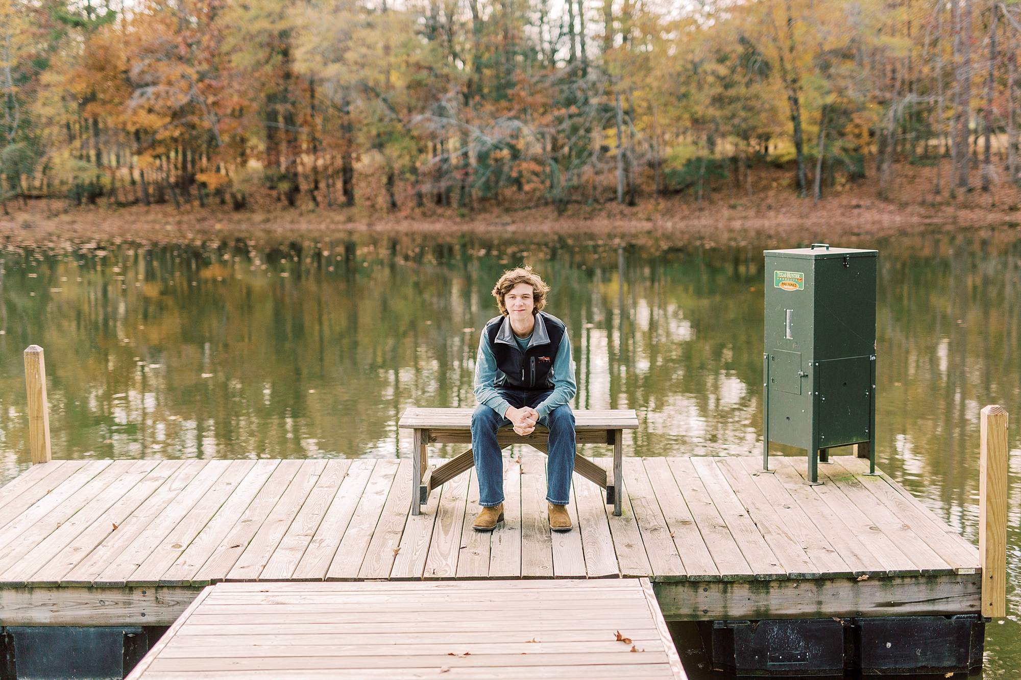 boy sits on wooden bench by lake during Midland NC senior portraits 