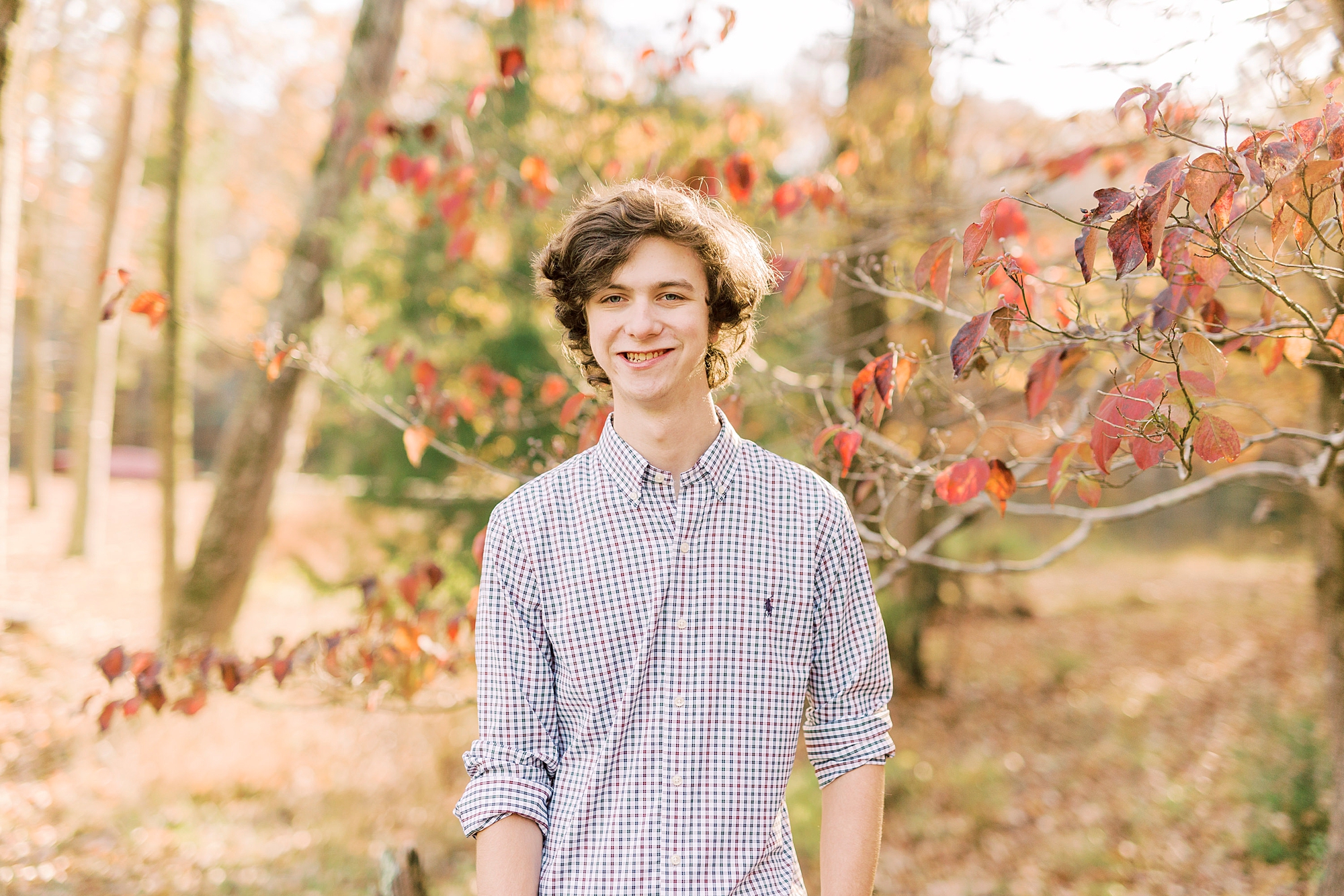 senior guy in button down shirt stands in fall foliage during Midland NC senior portraits 