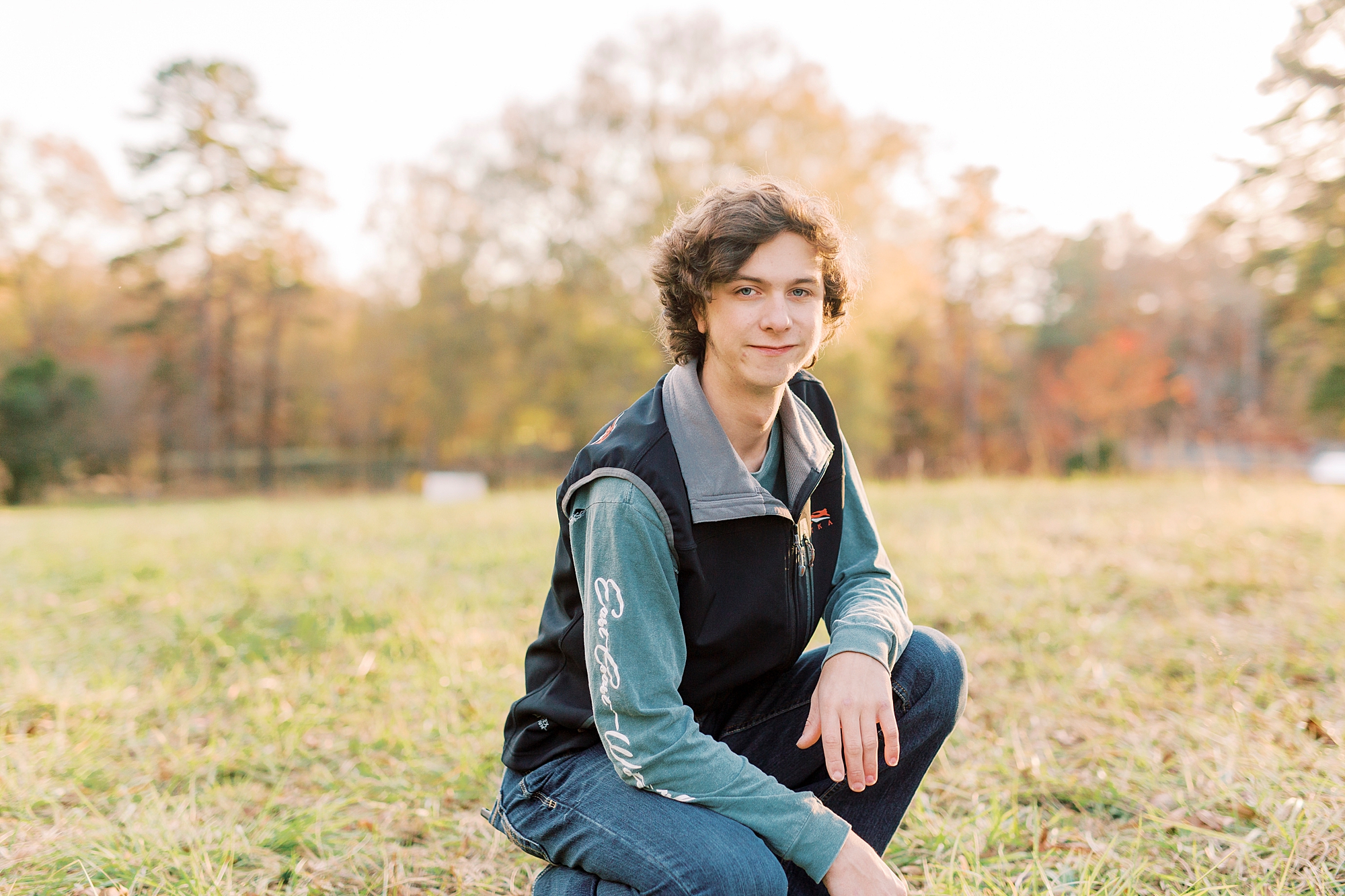 senior boy kneels down in grass during fall senior session in Midland NC