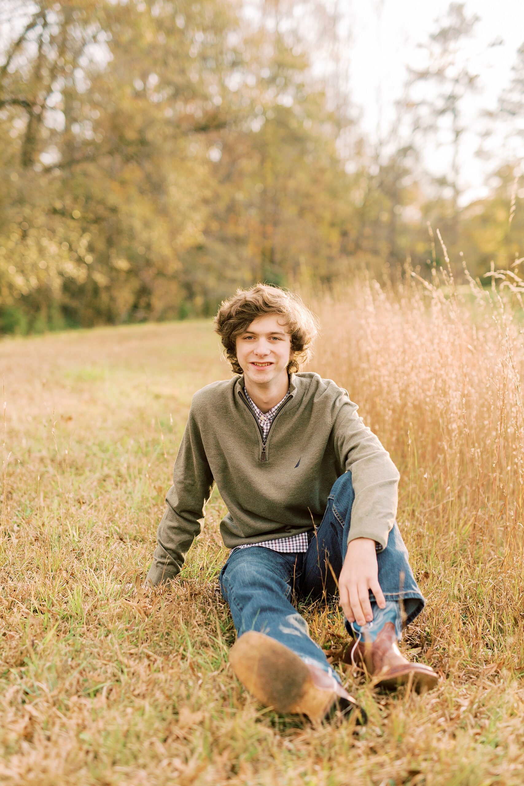 senior sits in grass with hand on his leg during fall Midland NC senior portraits 