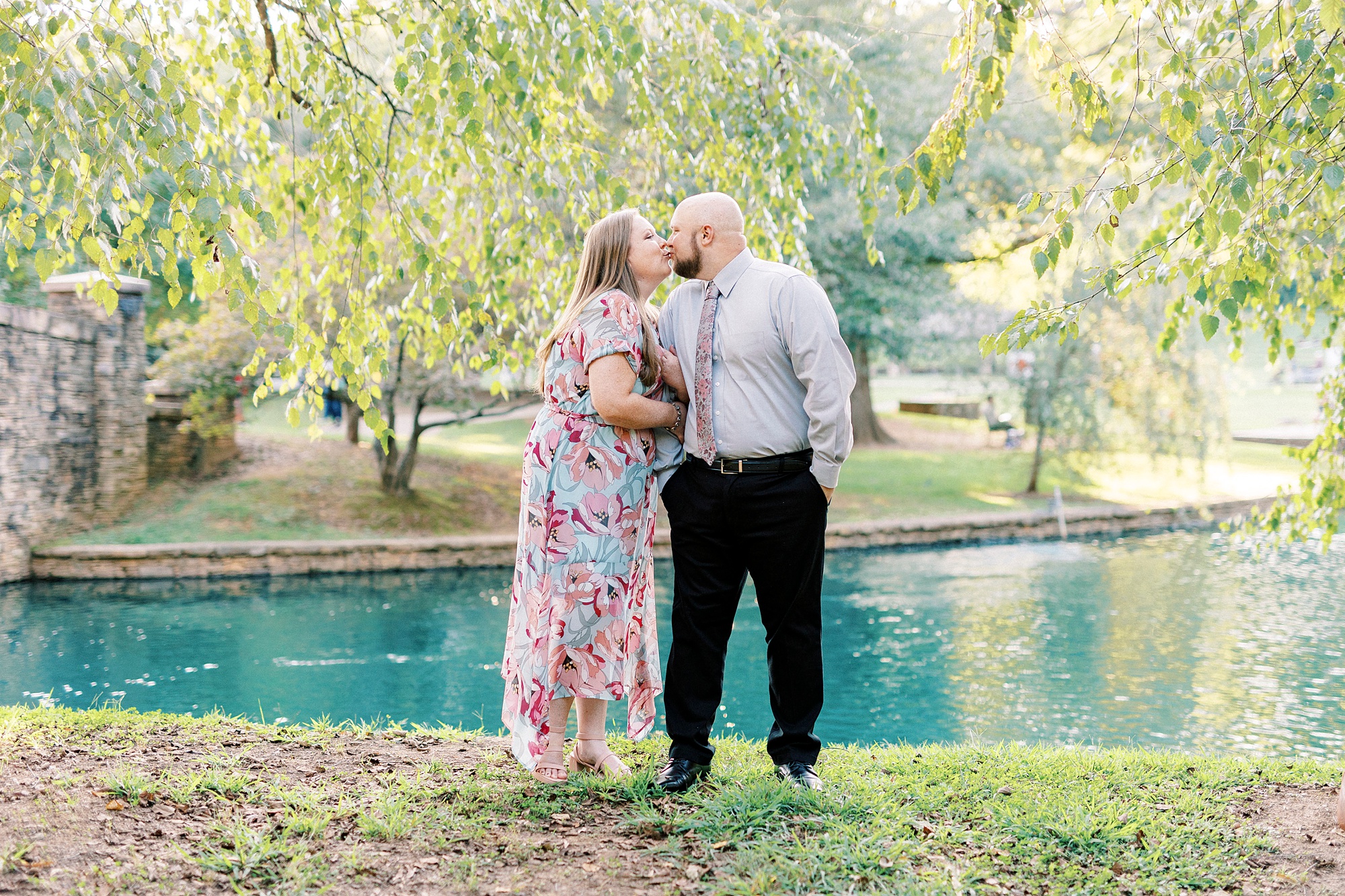 engaged couple kisses near pond under weeping willow during Freedom Park engagement portraits