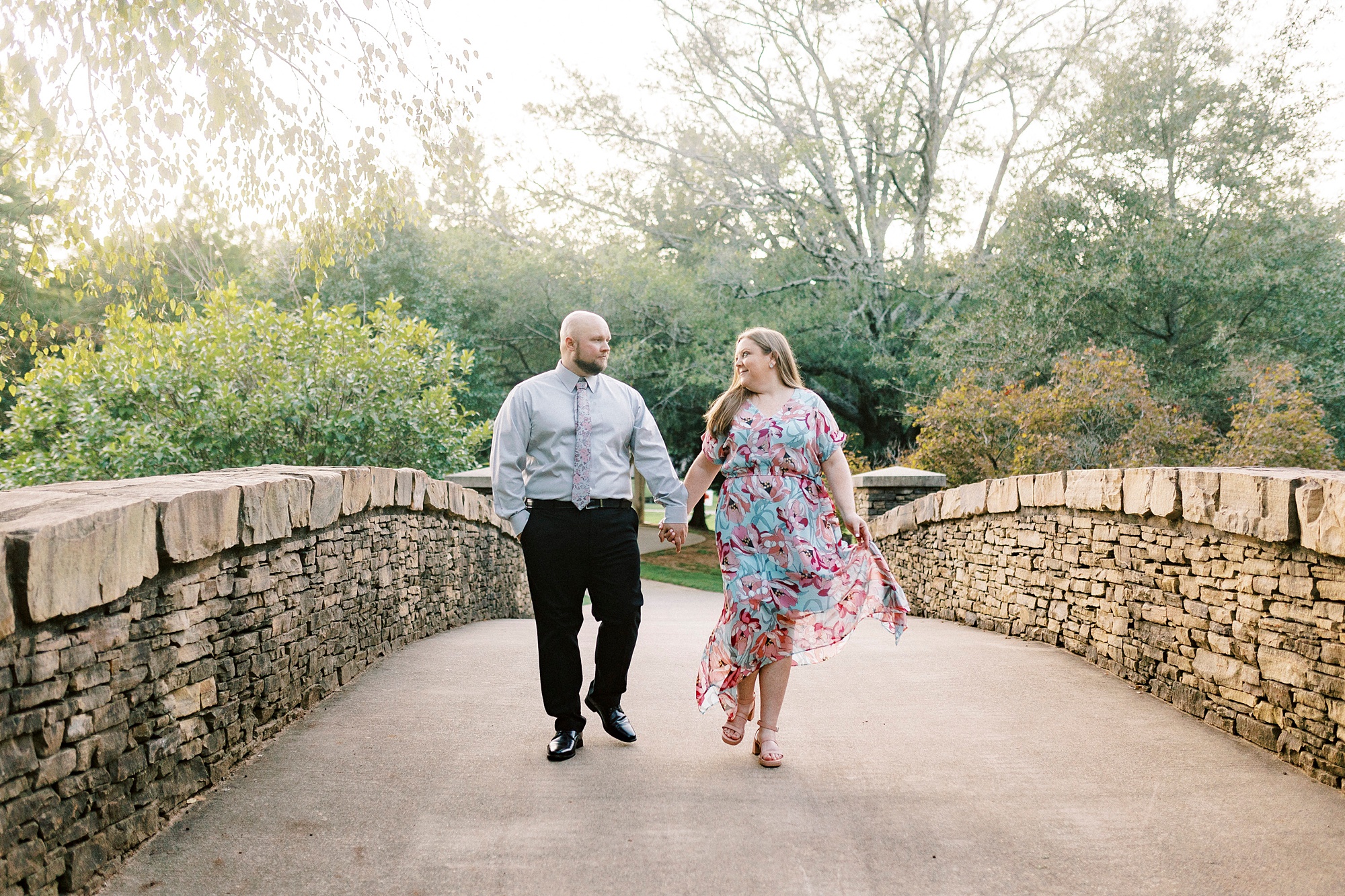 couple holds hands walking on stone bridge during Freedom Park engagement portraits