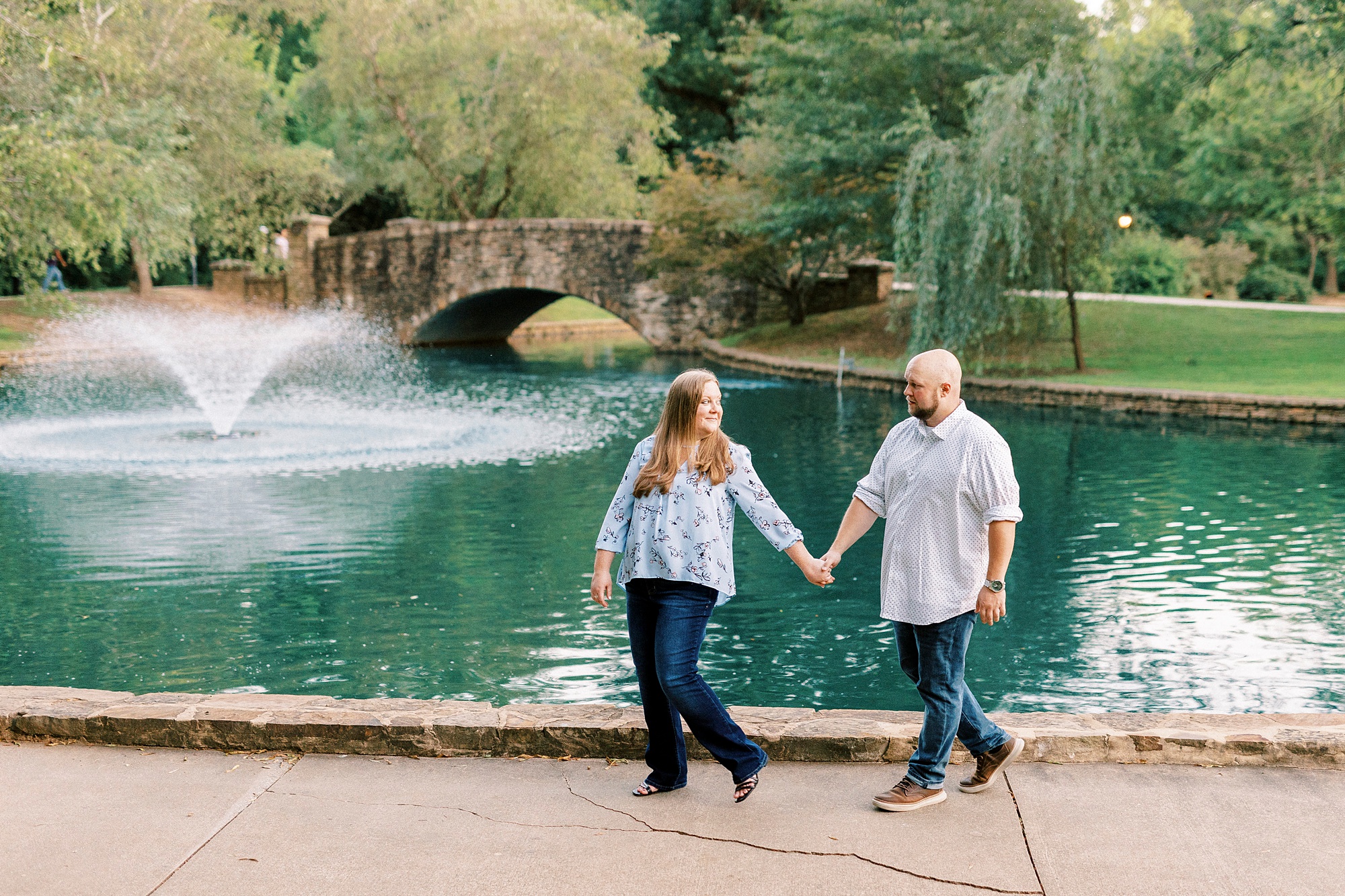 couple holds hands walking near pond with fountain in Freedom Park