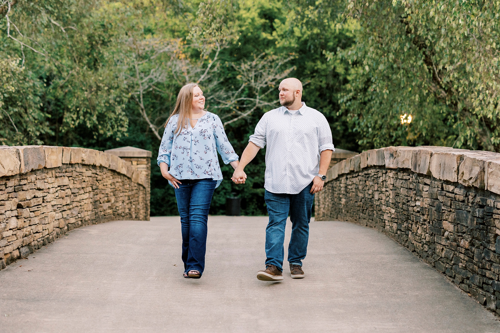 engaged couple holds hands walking on stone bridge during Freedom Park engagement portraits